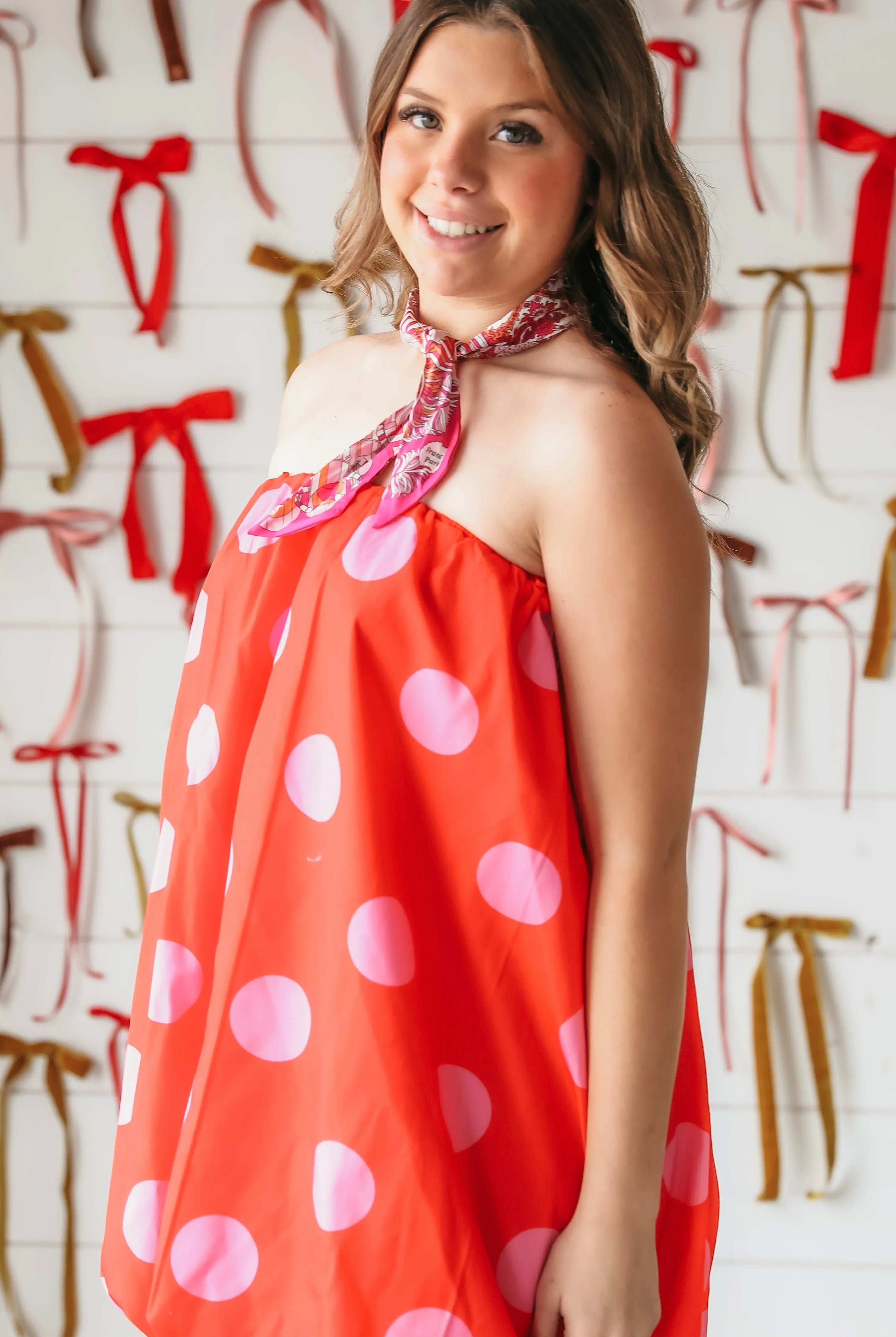 Red strapless bubble dress with pink polka dots, tied with a floral scarf. Model smiles at camera.