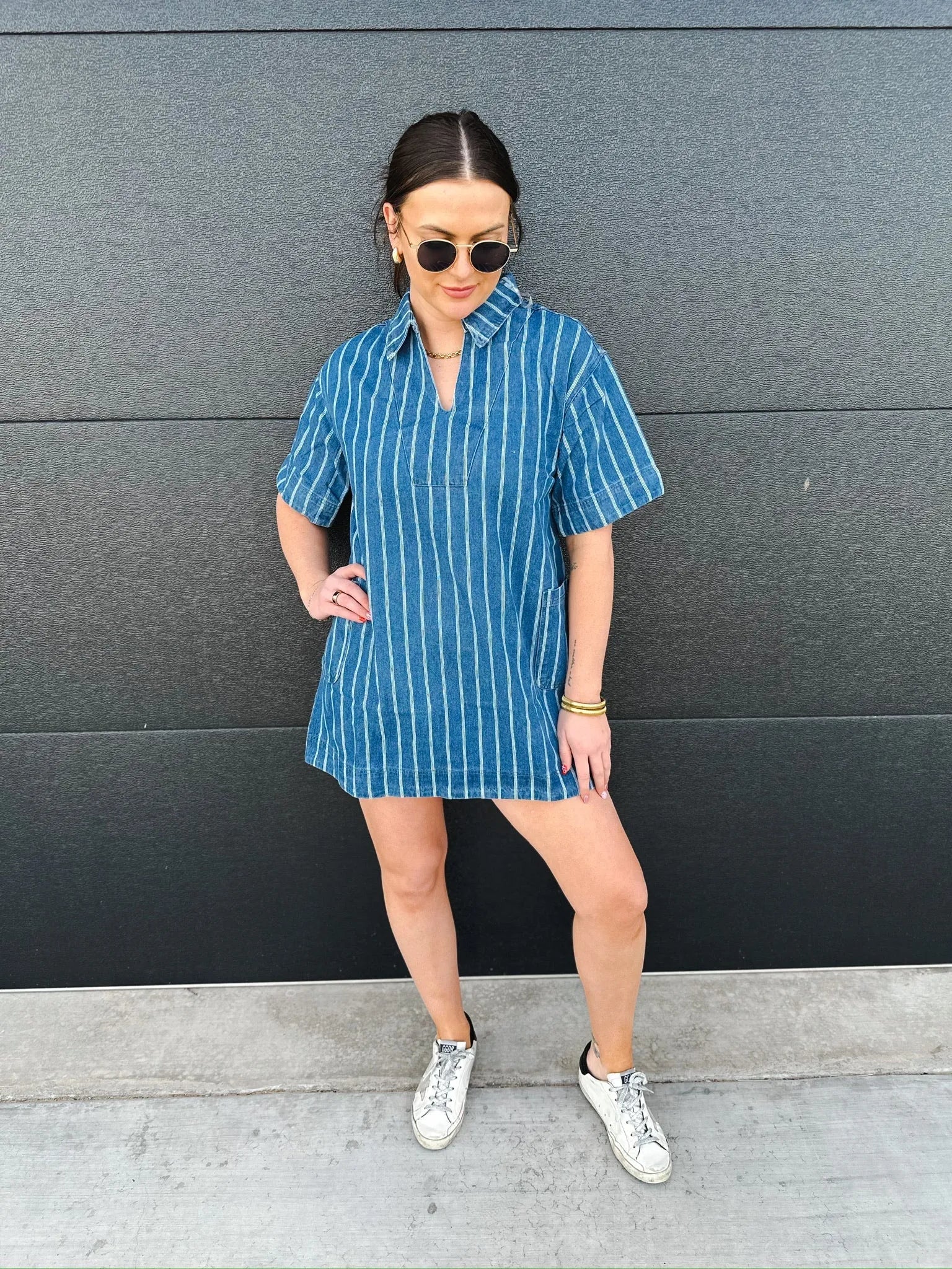 Woman wearing a short-sleeve denim dress with vertical white stripes and a split neckline, paired with white sneakers.