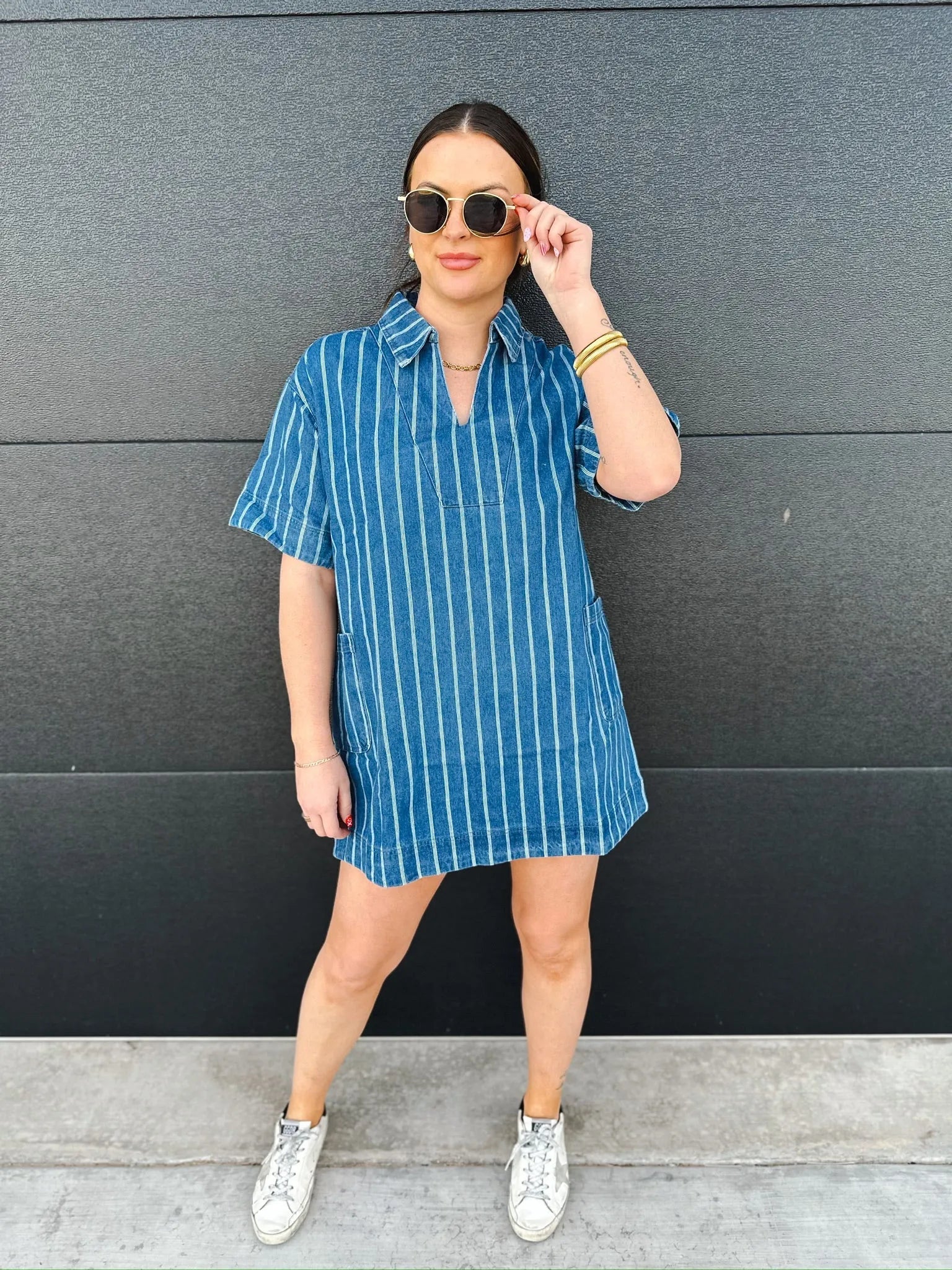 Woman wearing a relaxed fit short sleeve denim split neck dress with white vertical stripes. She has on sunglasses and