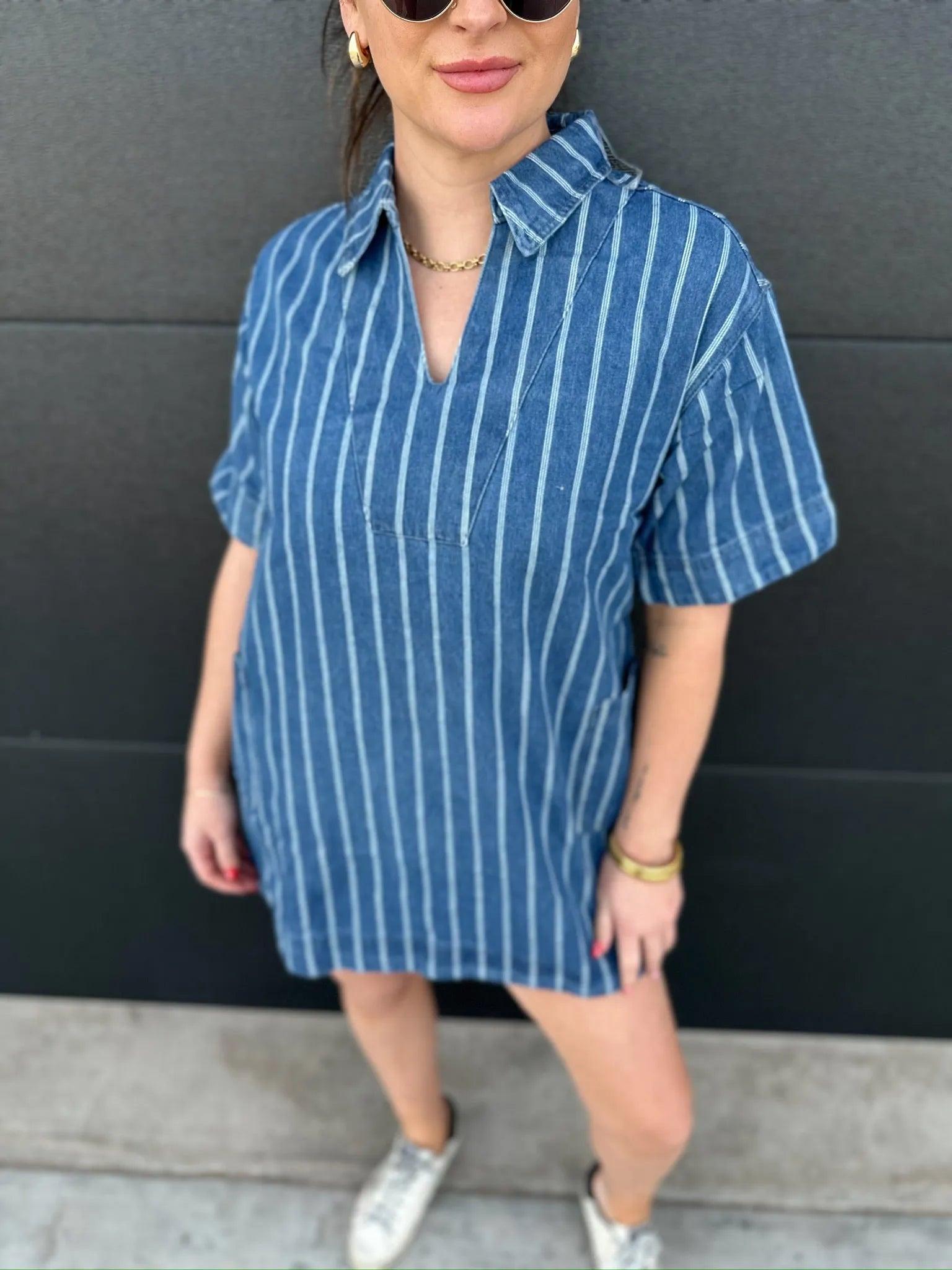 Woman wearing a short sleeve blue denim dress with vertical white pinstripes and a split neckline.