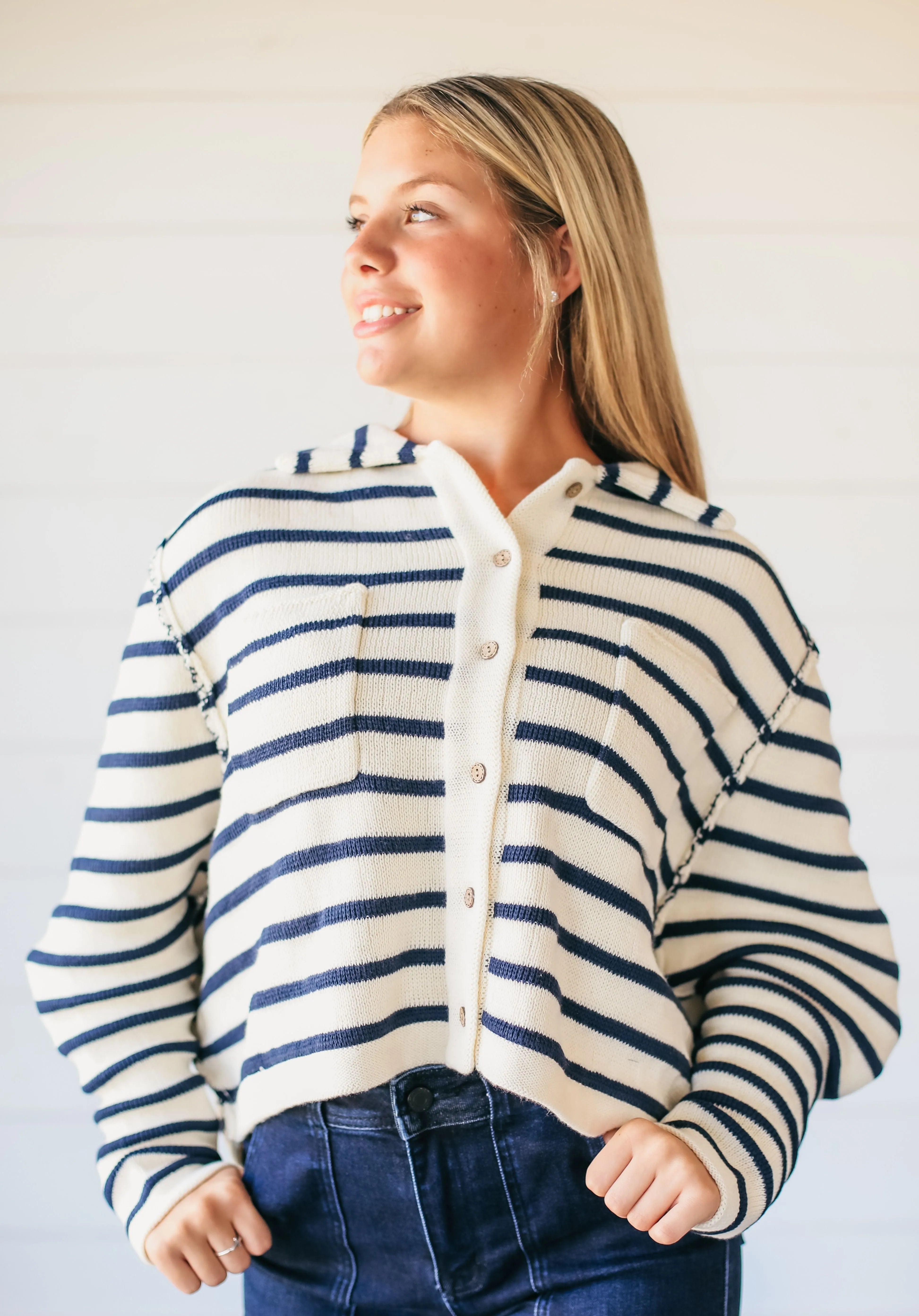 Woman wearing a relaxed fit, cream-colored button-down sweater with navy blue horizontal stripes and a collared neckline.