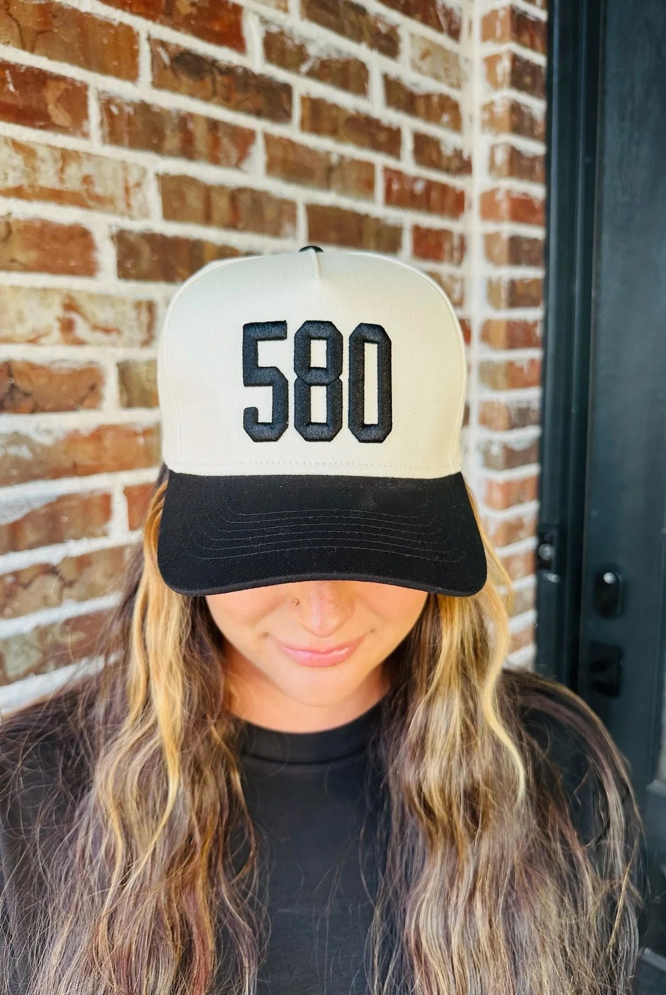 Black trucker hat with a cream front panel embroidered with "580" in black block letters. Black brim.