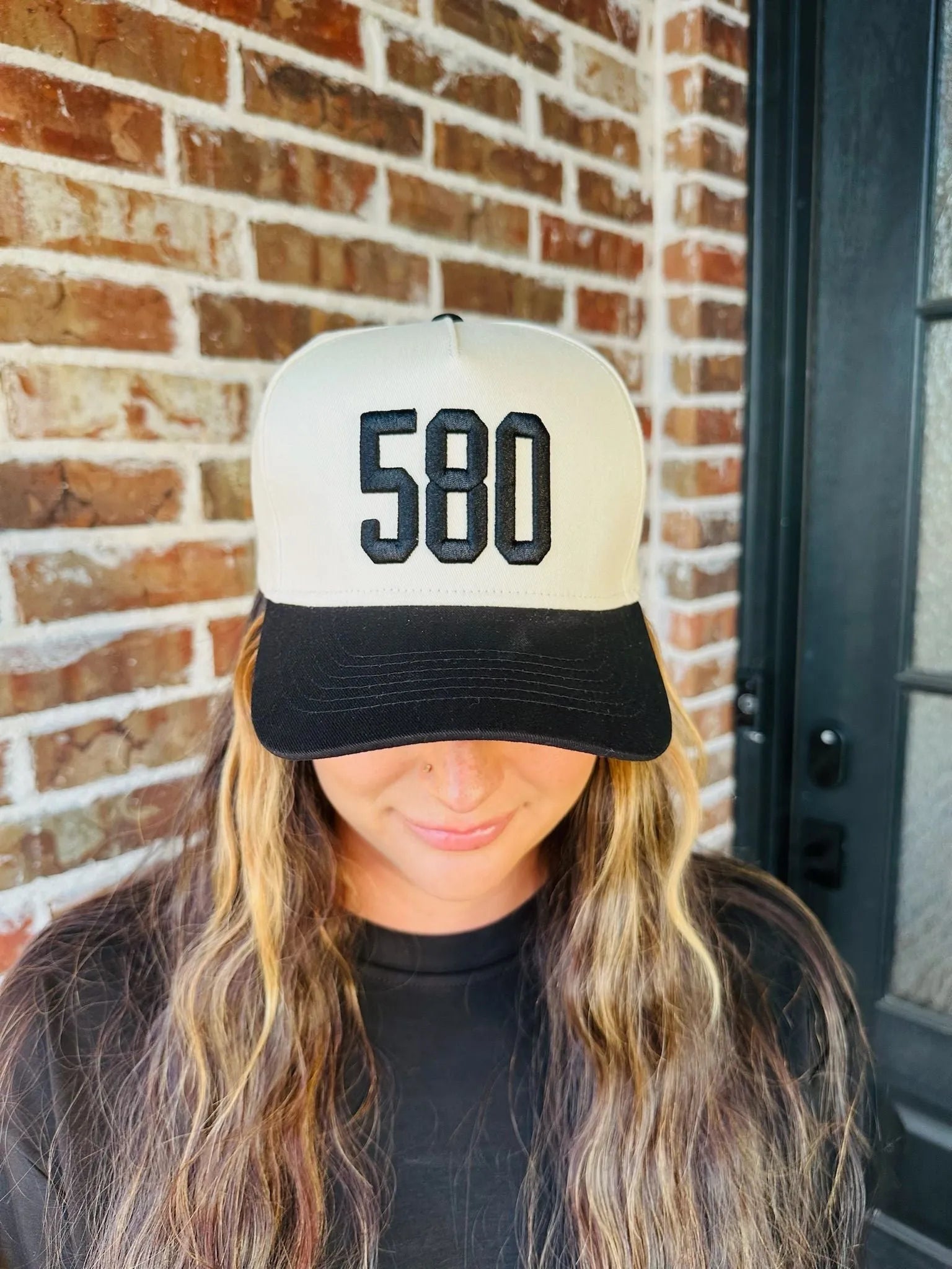 Black trucker hat with a cream front panel embroidered with "580" in black block letters. Black brim.