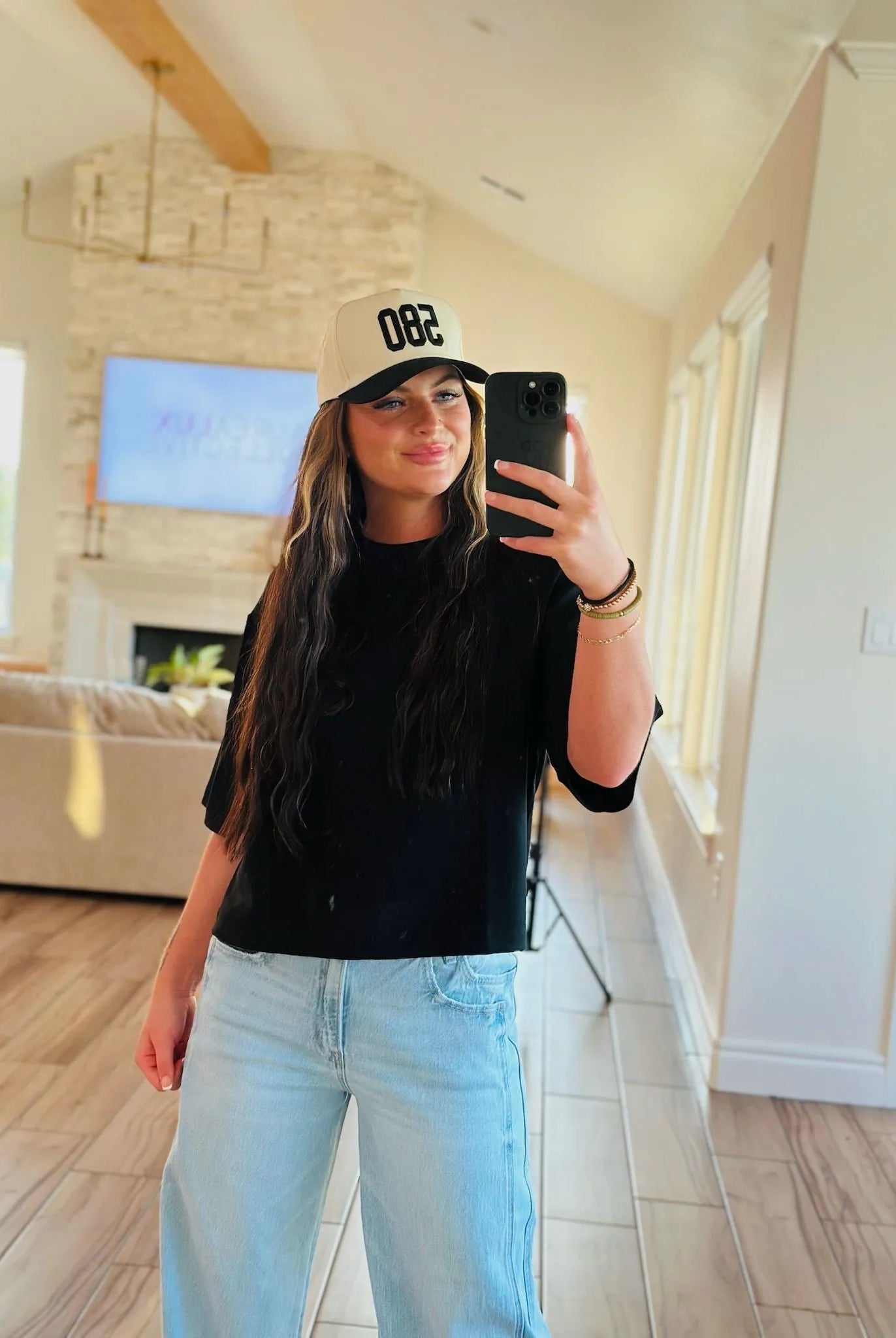 REPRESENT 580 trucker hat in black and beige with custom area code "082" on front. Woman wearing hat, black t-shirt, and