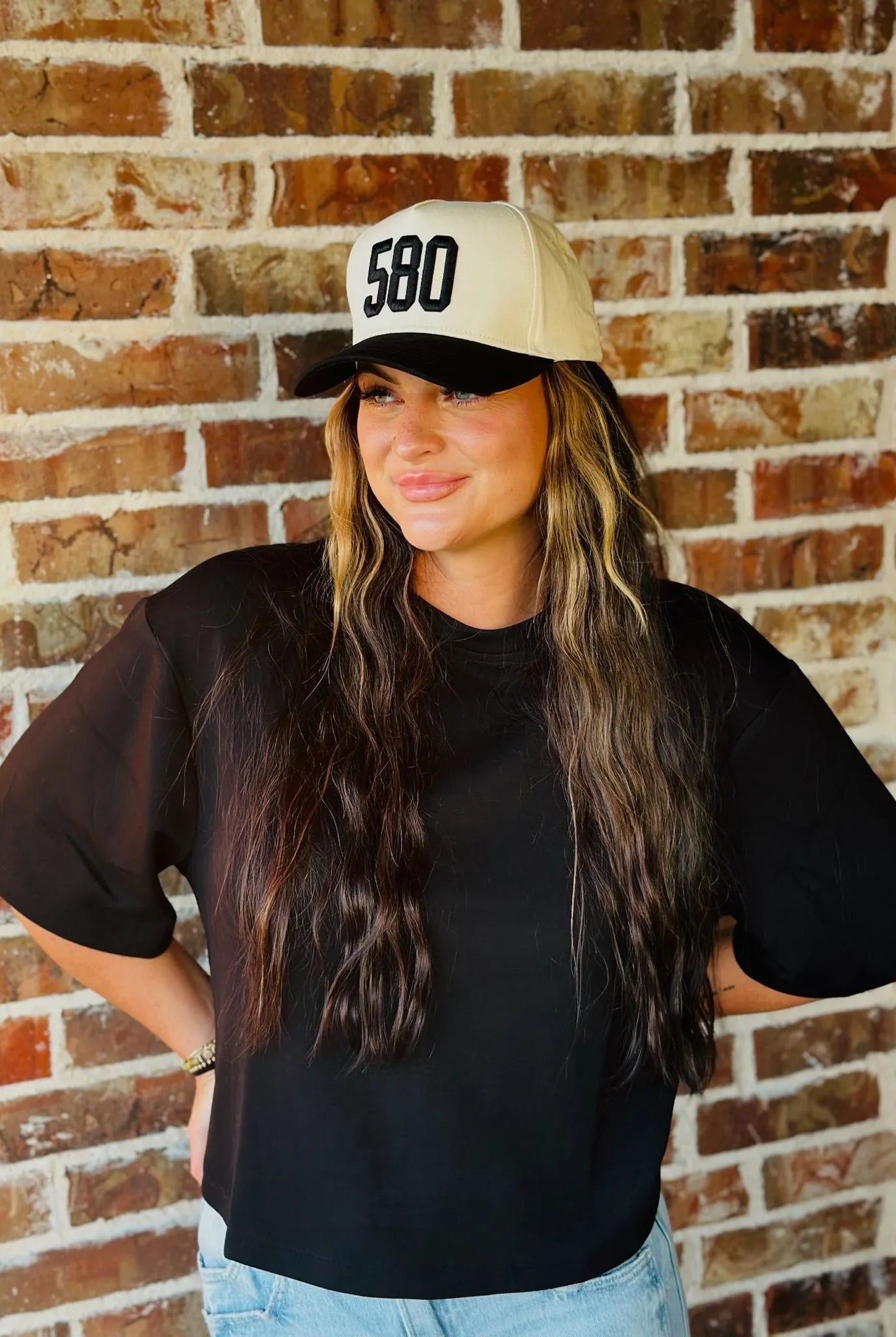 REPRESENT 580 custom area code trucker hat in black and off-white, worn by a woman with long brown hair.