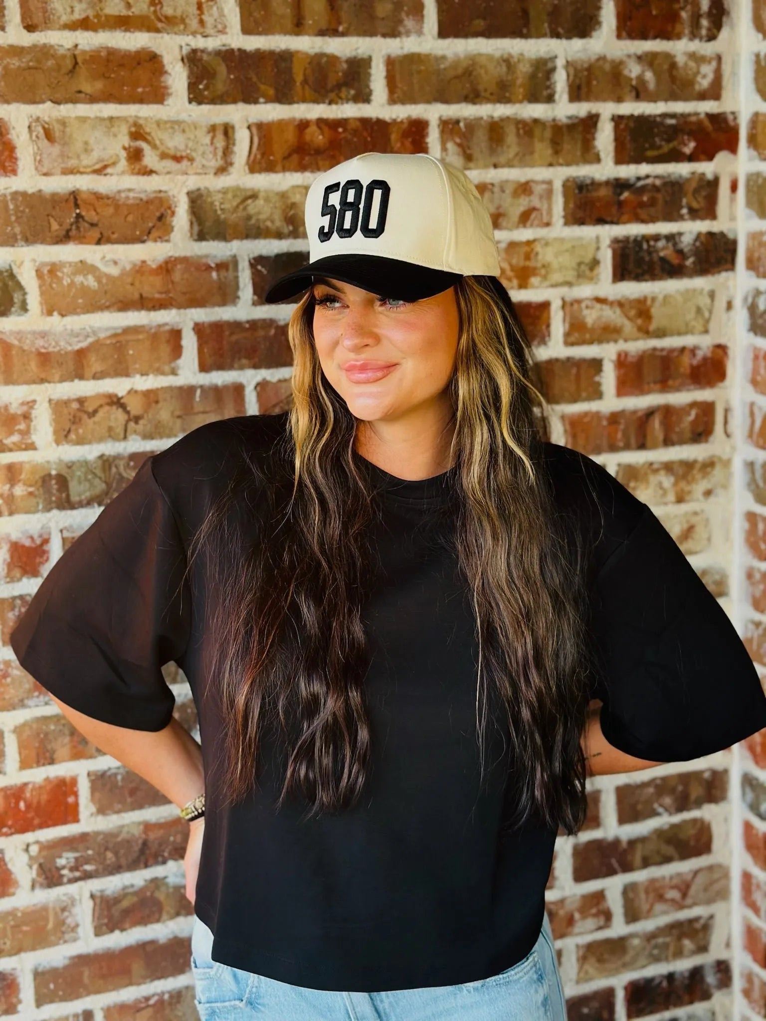 REPRESENT 580 custom area code trucker hat in black and off-white, worn by a woman with long brown hair.