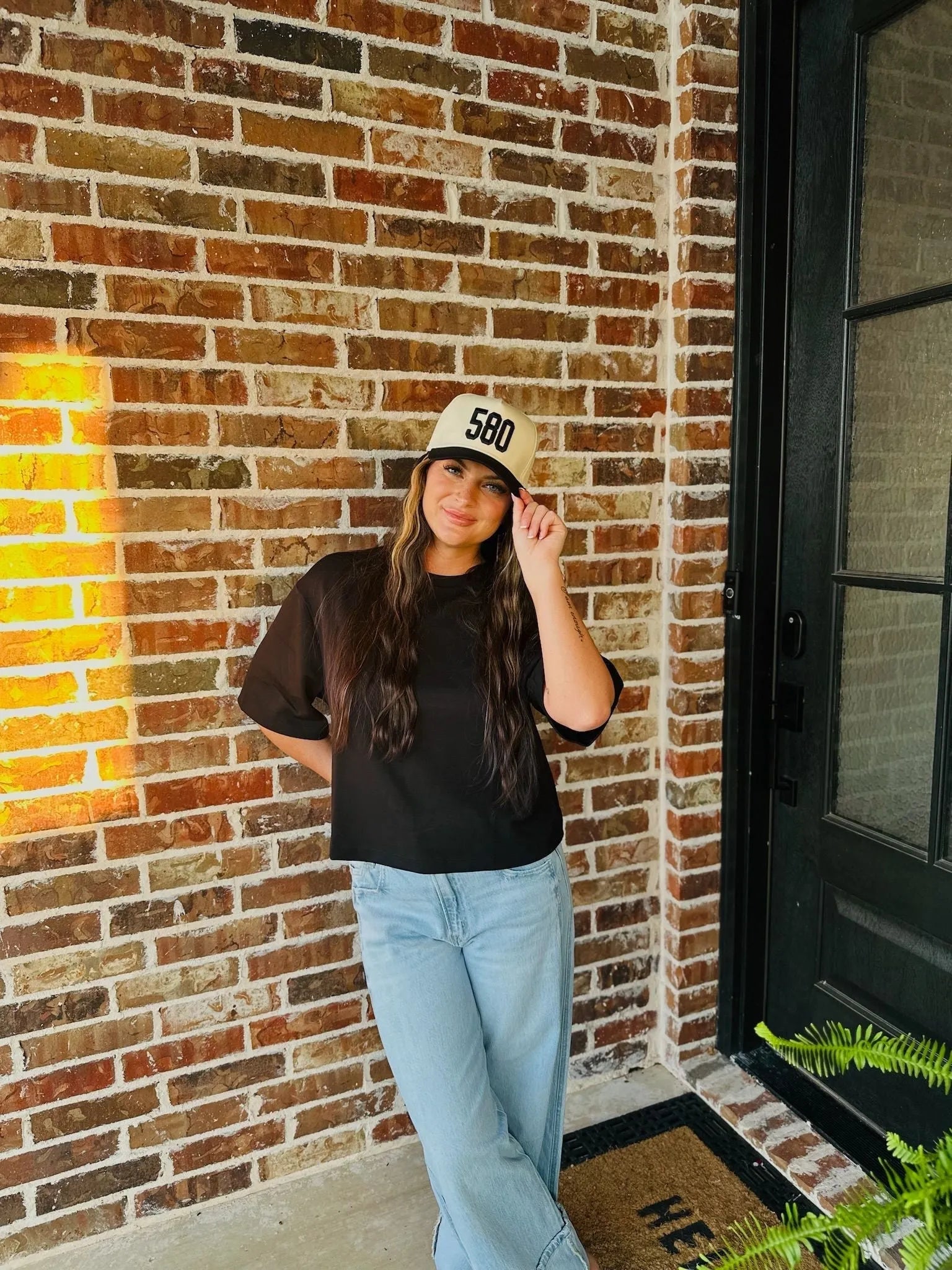 Woman wearing a black REPRESENT 580 custom area code trucker hat on a brick background.