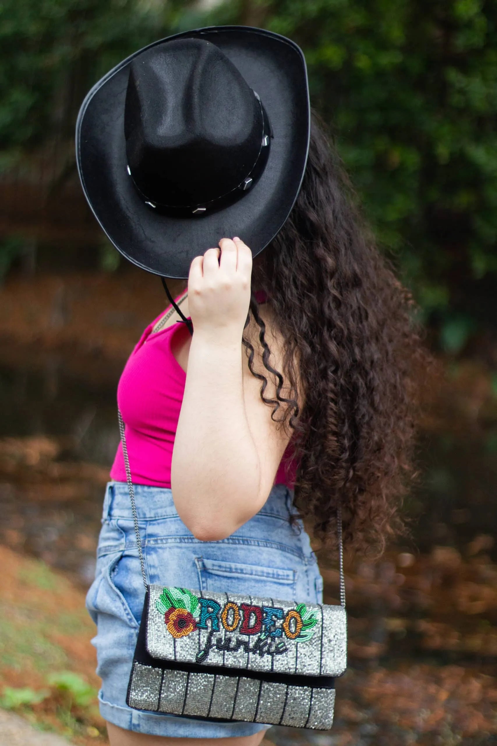 Rodeo Junkie beaded clutch purse with colorful floral and text embroidery, silver beaded front. Model wears pink tank top