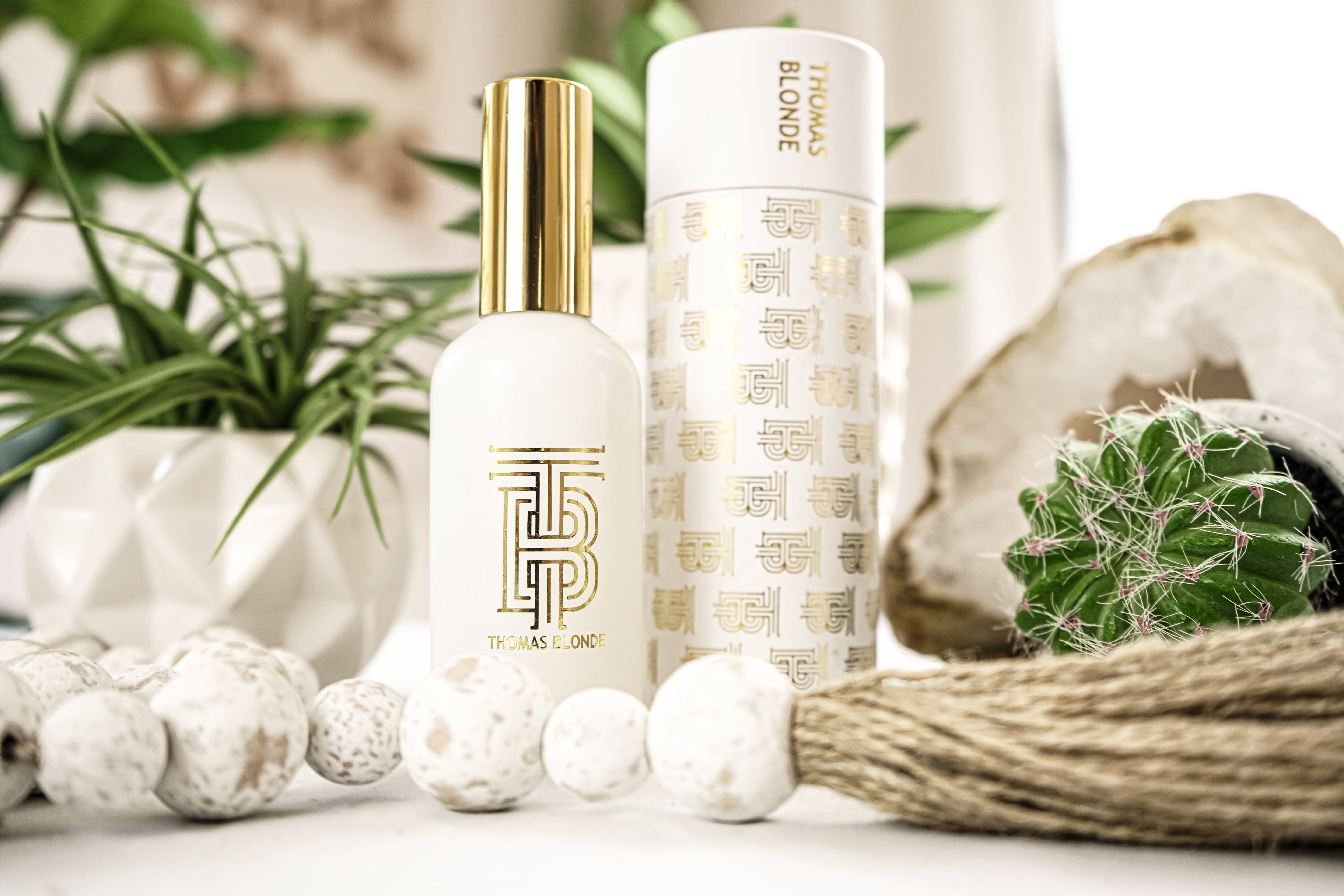 White Room and Linen Refresh Spray bottle with gold cap and logo by Thomas Blonde, next to matching cylindrical packaging