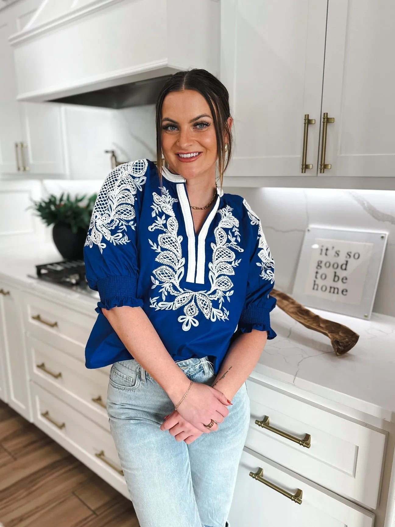 Woman wearing a royal blue V-neck top with white embroidery and puff sleeves, paired with light wash jeans.