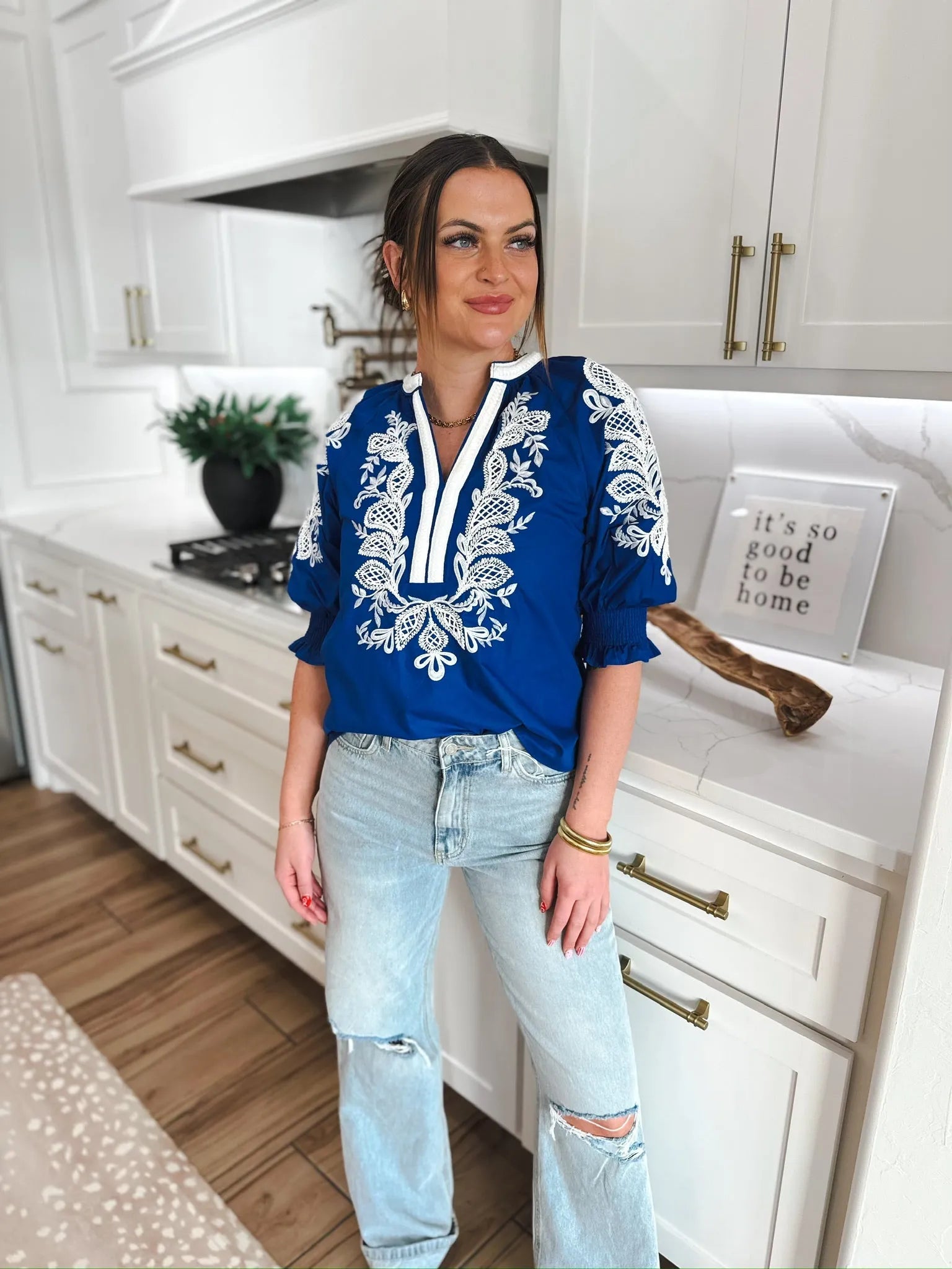 Royal blue top with white embroidery on V-neck and puff sleeves. Model wears light wash ripped jeans.