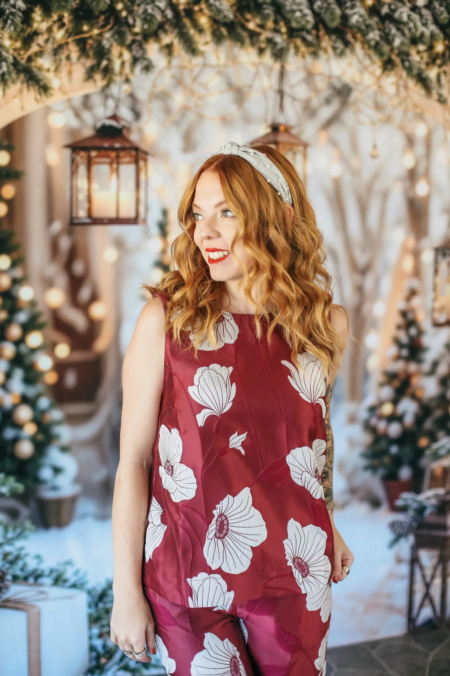 Woman in burgundy floral print business casual set, sleeveless top with white flowers, matching pants. Festive background.