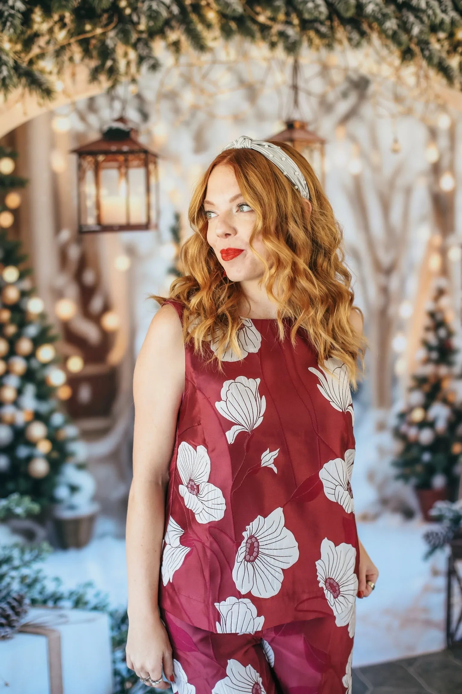 Woman wearing a ruby red sleeveless top with a white floral print and matching pants, adorned with a pearl headband