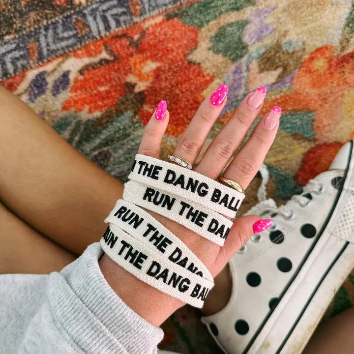 White embroidered bracelet with black text reading 'THE DANG BALL RUN THE DANG BALL' wrapped around a wrist.