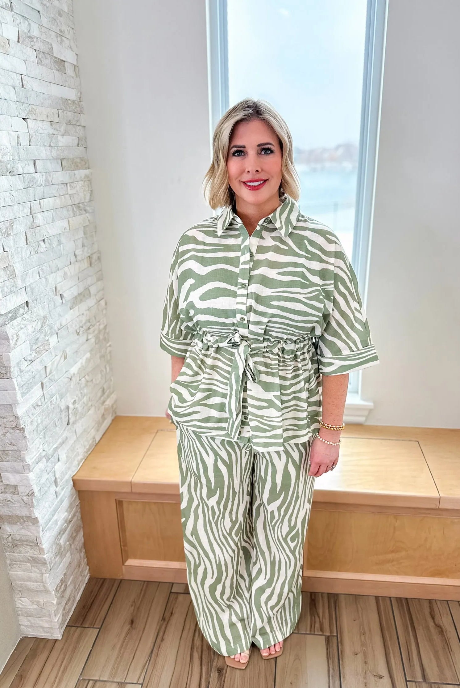 Woman wearing a sage green and cream zebra print matching set, featuring a belted shirt and wide-leg pants.