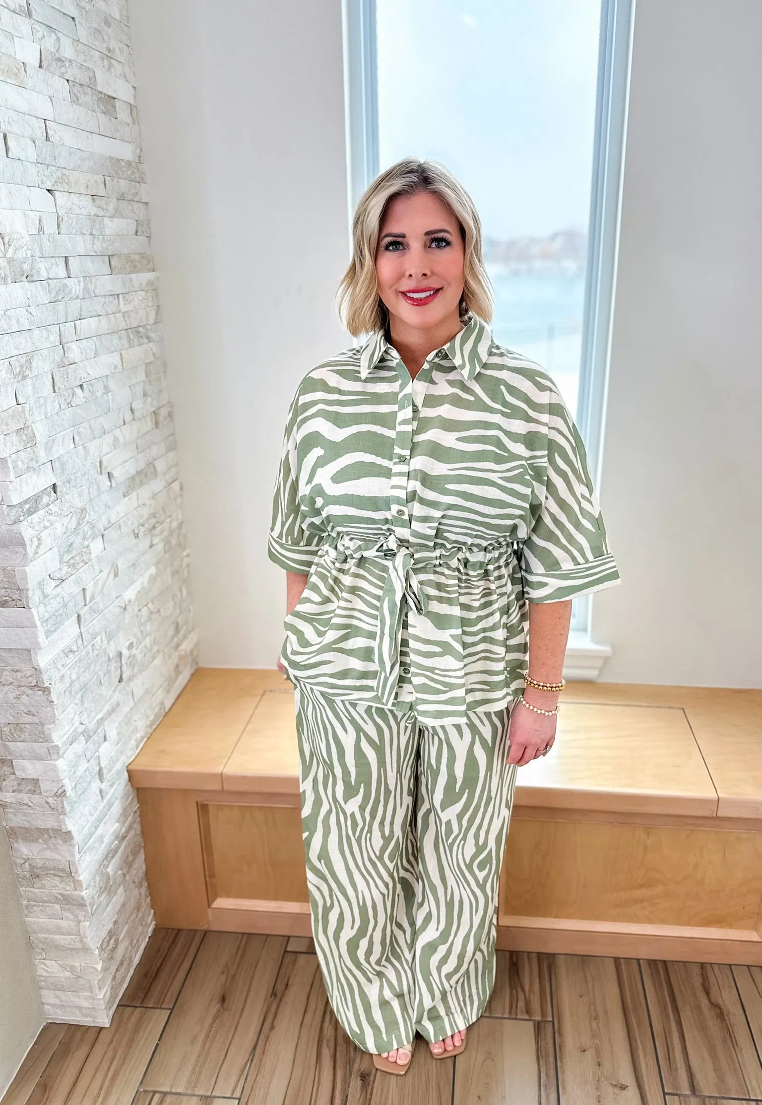 Woman wearing a sage green and cream zebra print matching set, featuring a belted shirt and wide-leg pants.