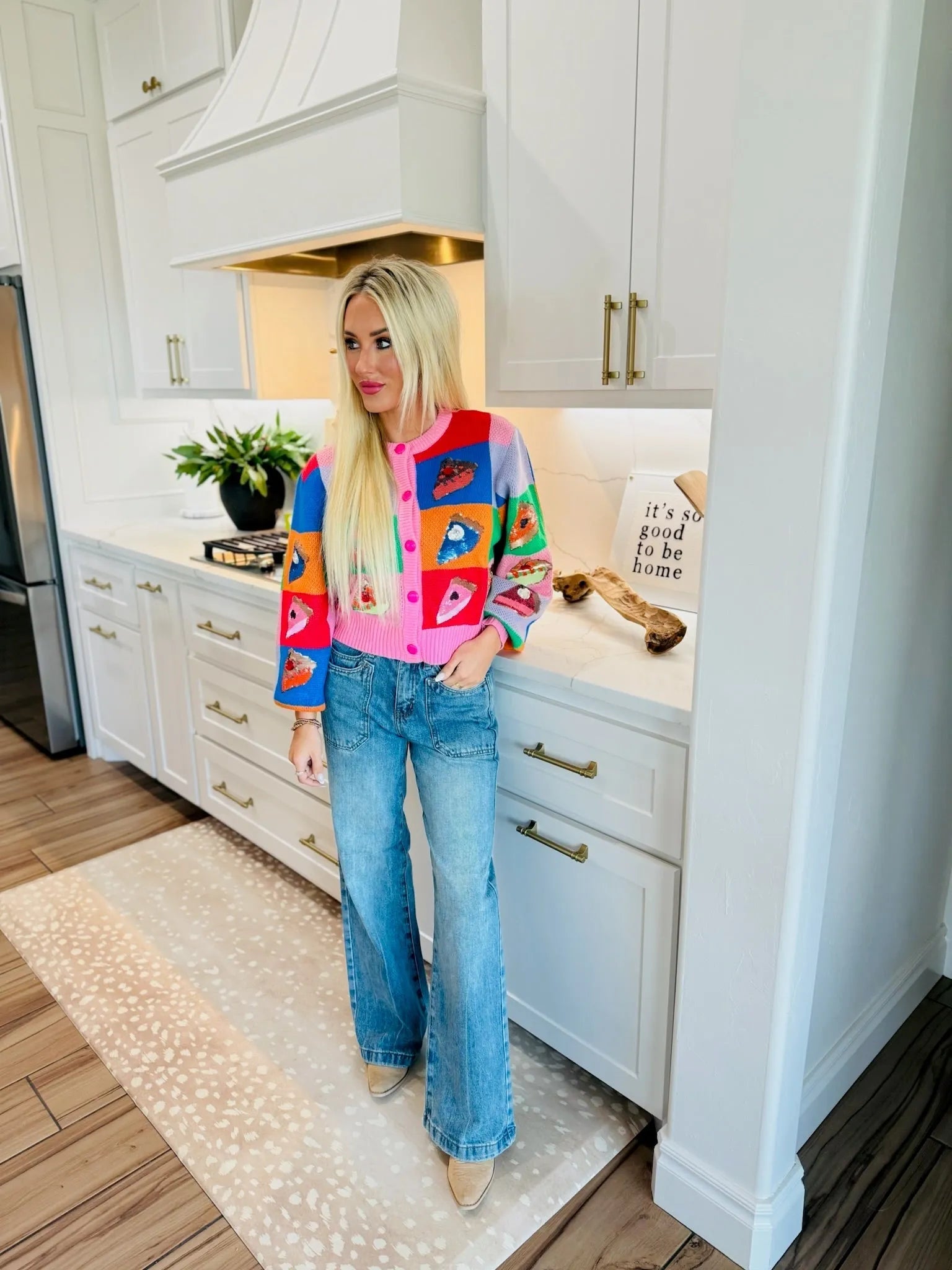 Woman in high-rise wide-leg jeans and a colorful cardigan with a pie slice pattern stands in a modern kitchen.