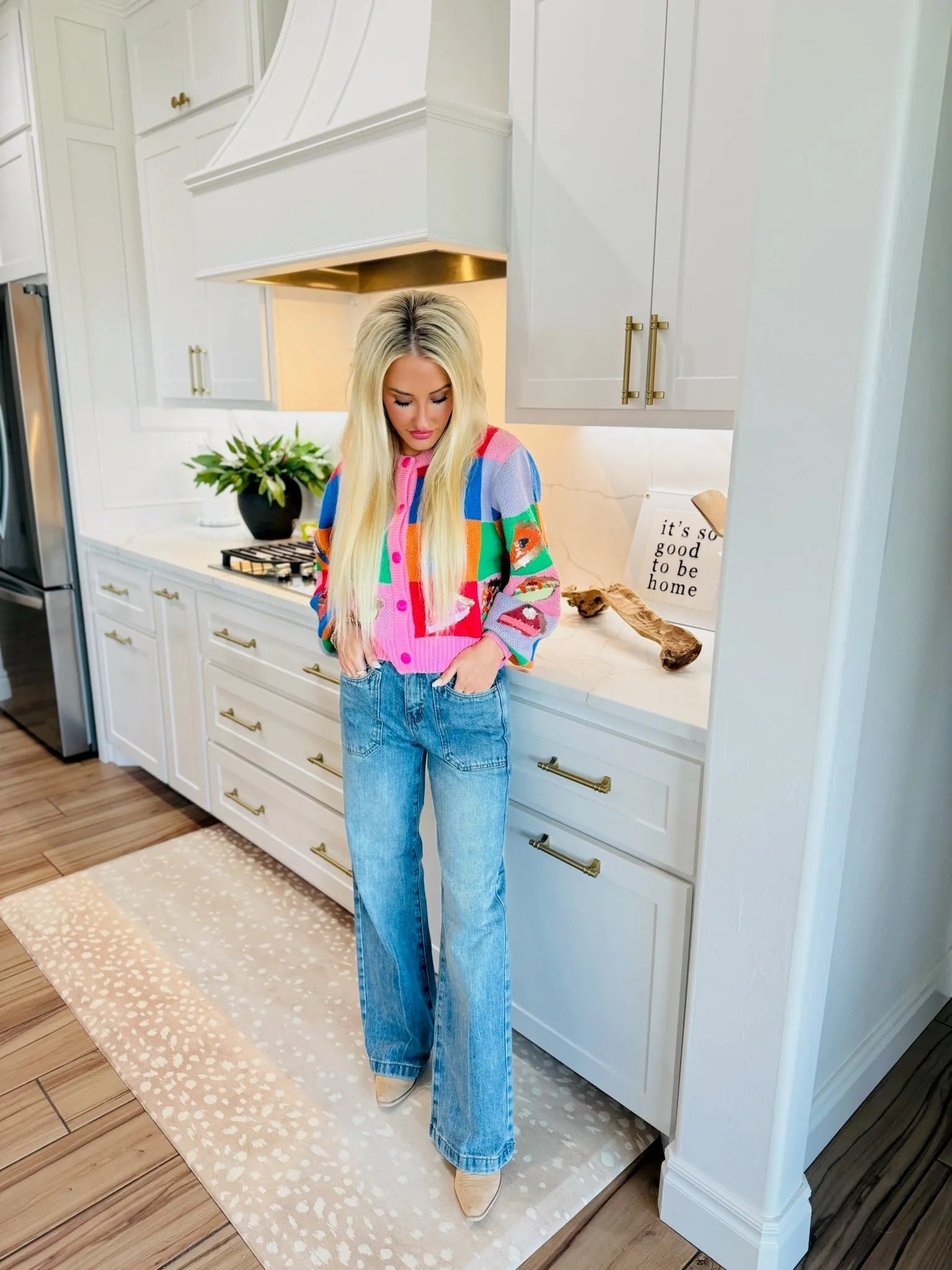 Woman wearing SAIGE high-rise double-pocket wide-leg jeans and a colorful patchwork cardigan in a kitchen.