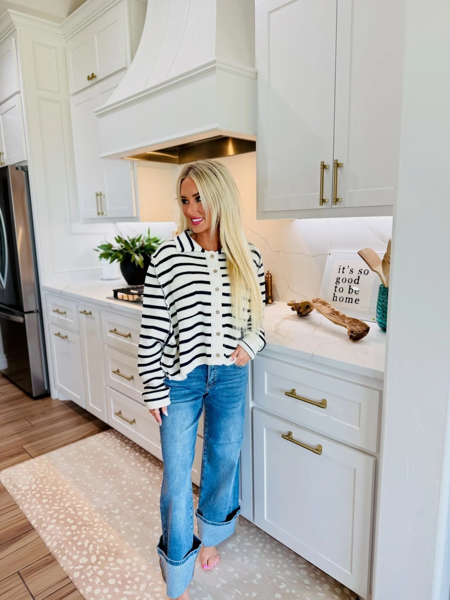 Woman wearing SAIGE mid-rise wide-leg jeans and a striped cardigan, standing in a modern kitchen.