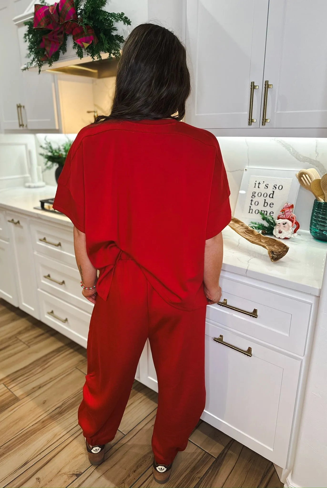 Woman wearing a solid red round neck top and semi harem pants set, standing in a kitchen.