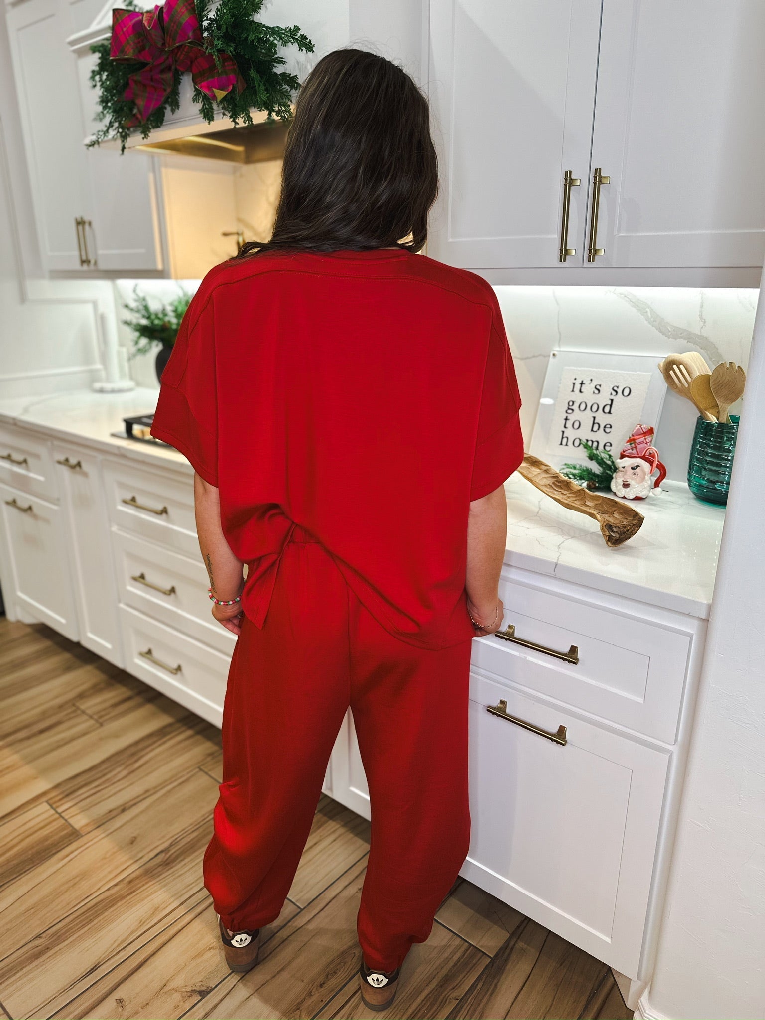Woman wearing a solid red round neck top and semi harem pants set, standing in a kitchen.