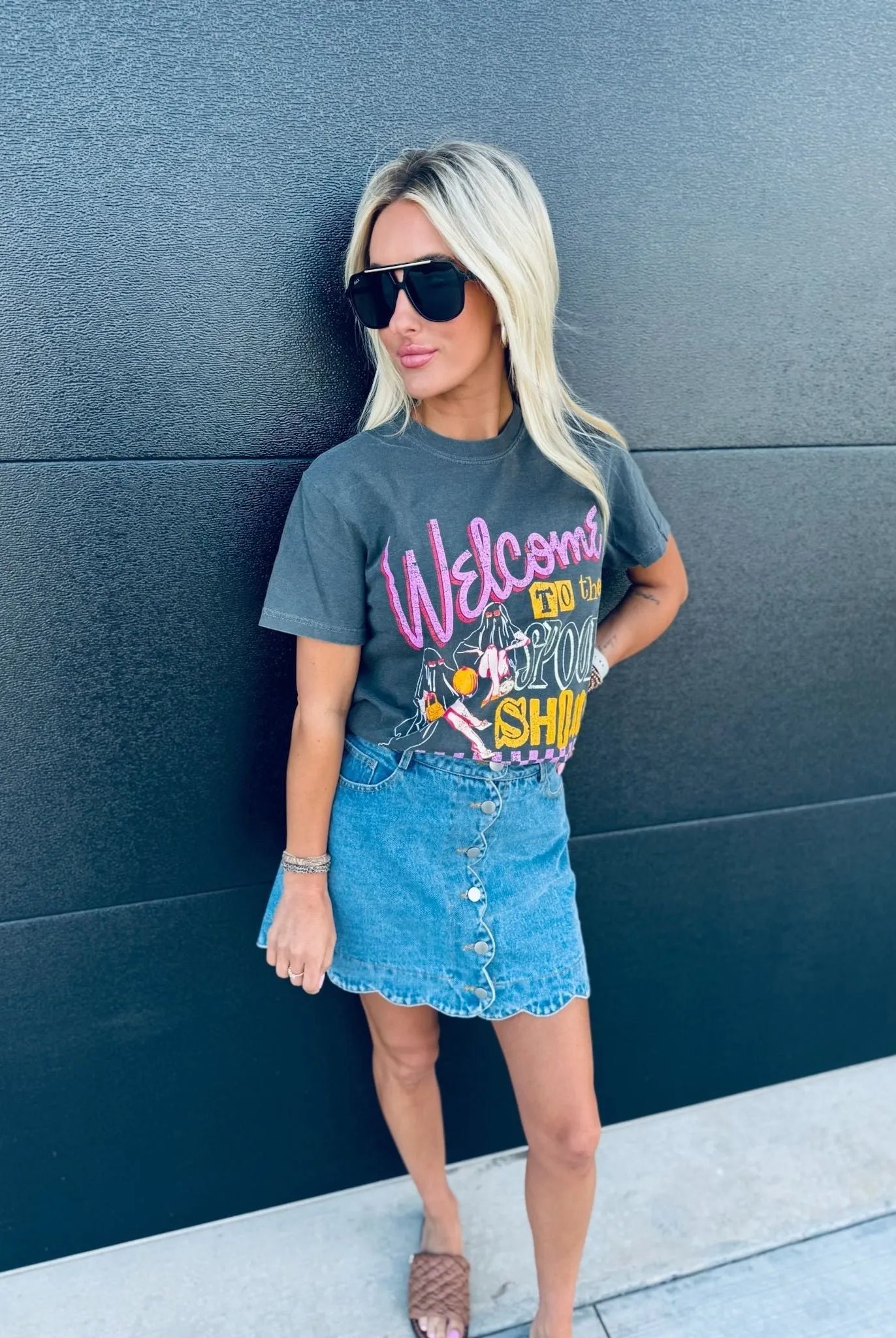 Woman wearing a dark gray Spook Show Halloween T-shirt with pink text and graphic art, paired with a denim skirt.
