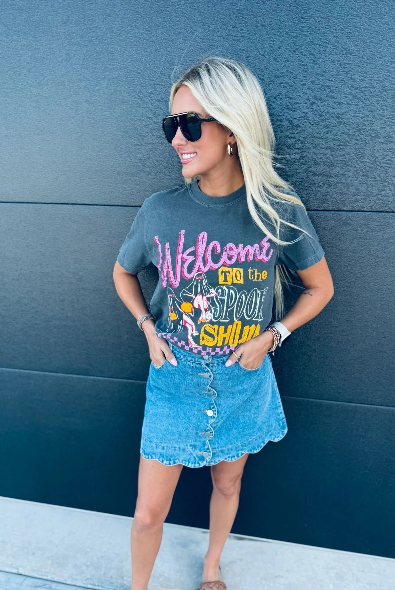 Woman wearing a charcoal gray Spook Show Halloween t-shirt with "Welcome to the Spook Show" graphic, paired with a denim