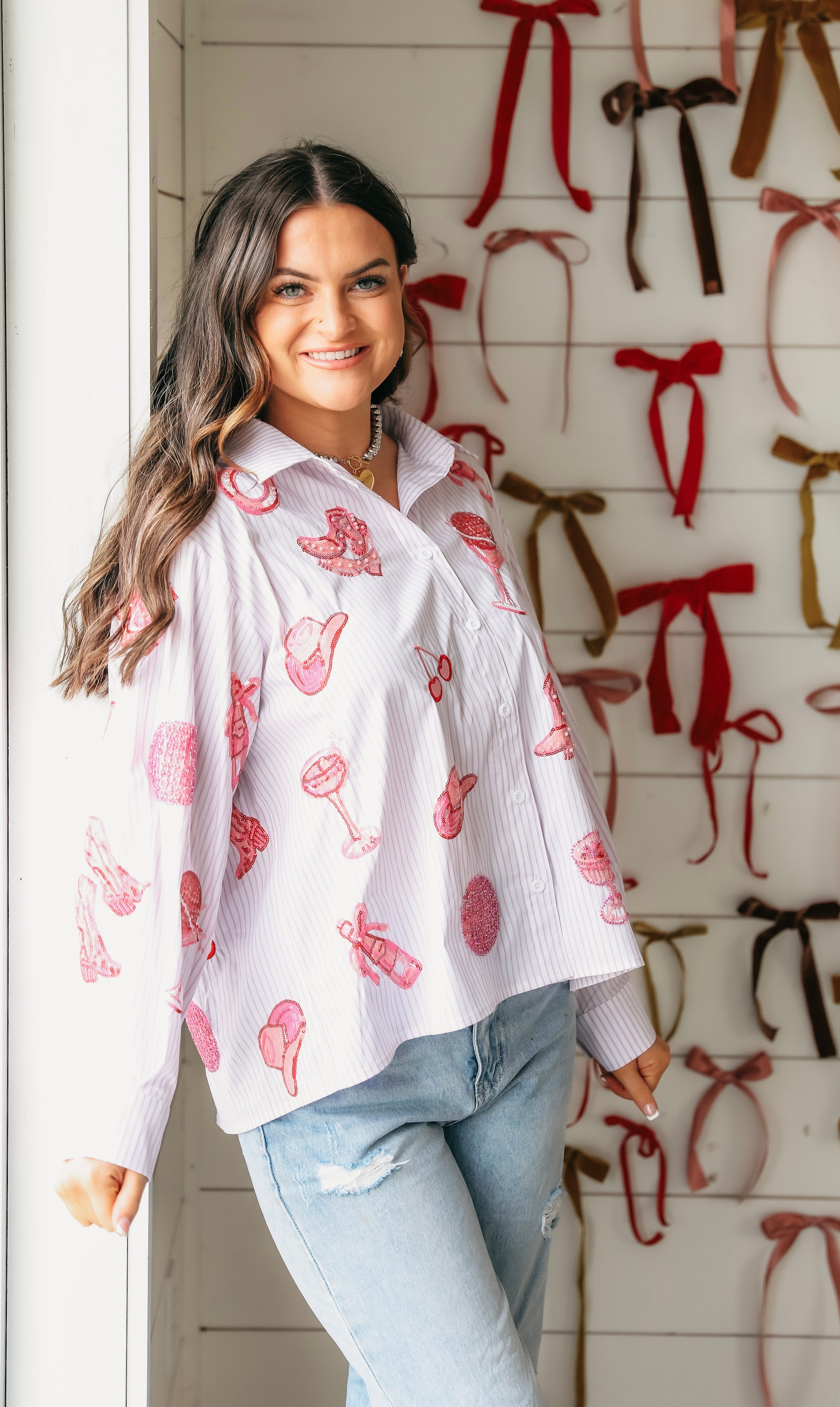 White collared shirt with thin pink pinstripes and an all-over print of pink disco cowgirl motifs like boots, hats, and