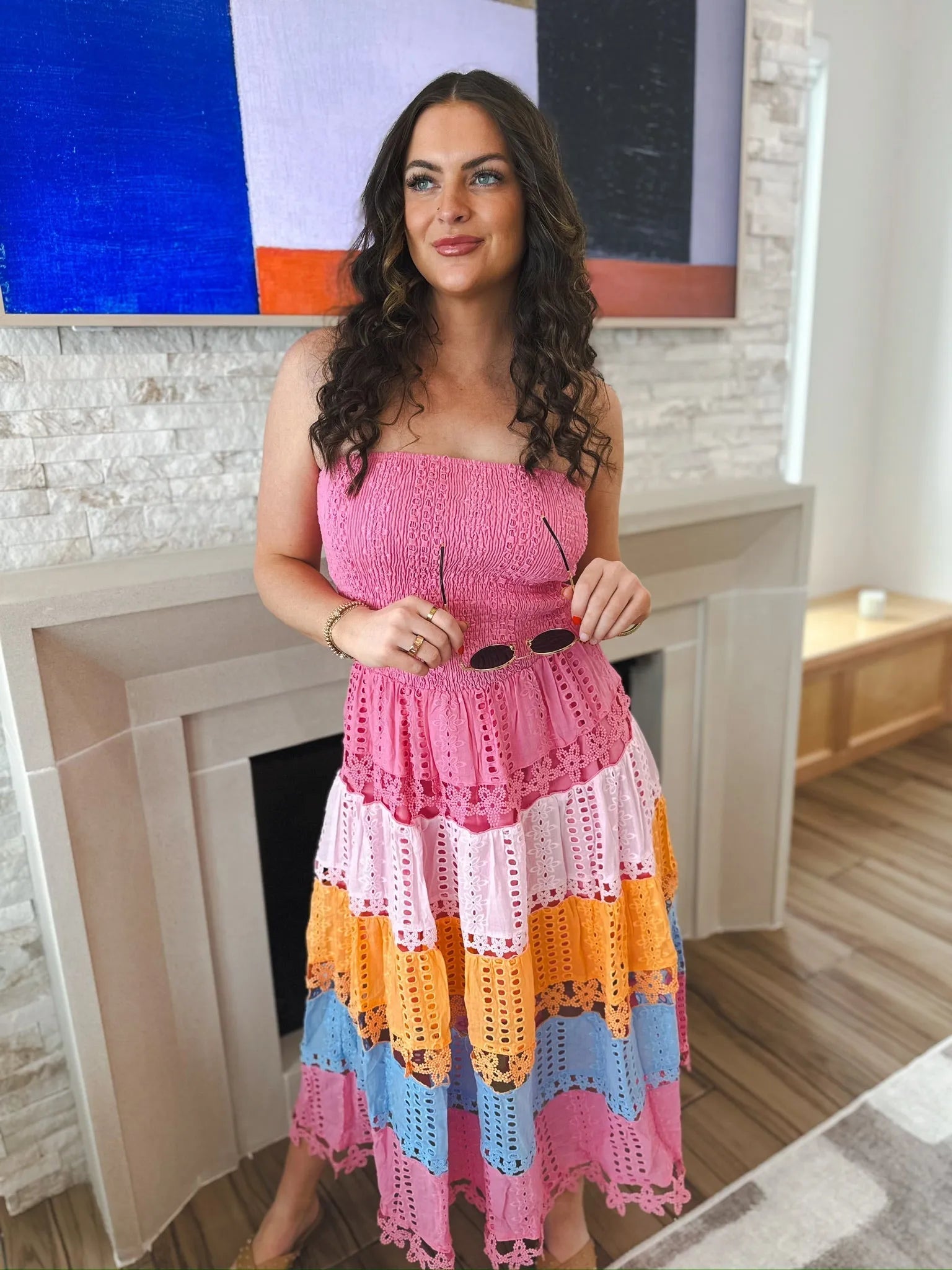 Woman in a pink strapless midi dress with multi-colored eyelet lace tiers: pink, light pink, orange, and blue. Holds
