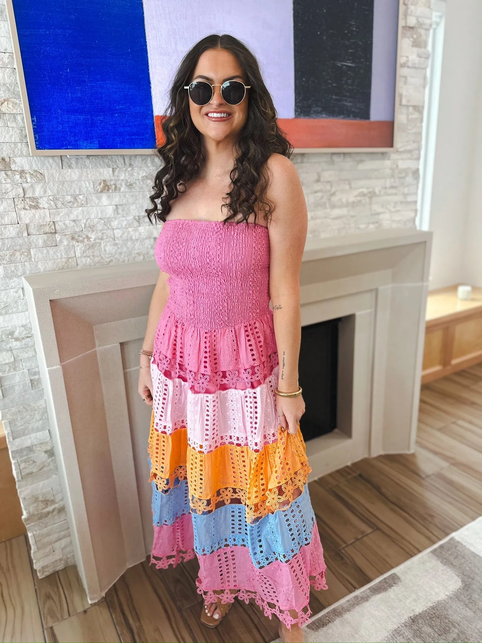 Woman wearing a pink strapless midi dress with colorful eyelet lace tiers in pink, orange, and blue. She has curly hair and