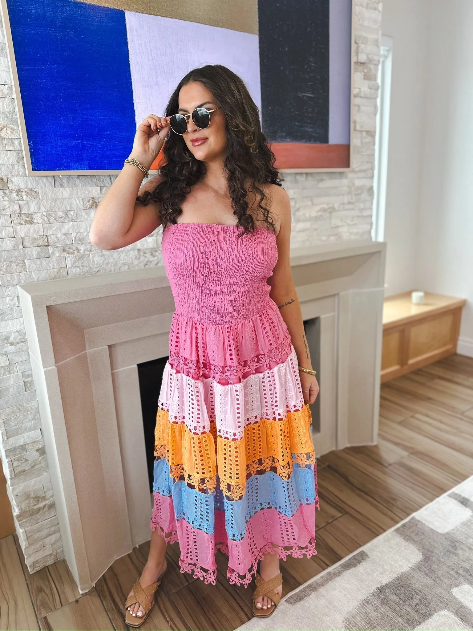 Model wearing a pink multi-eyelet lace midi dress with smocked bodice and tiered skirt in pink, peach, orange, and blue.