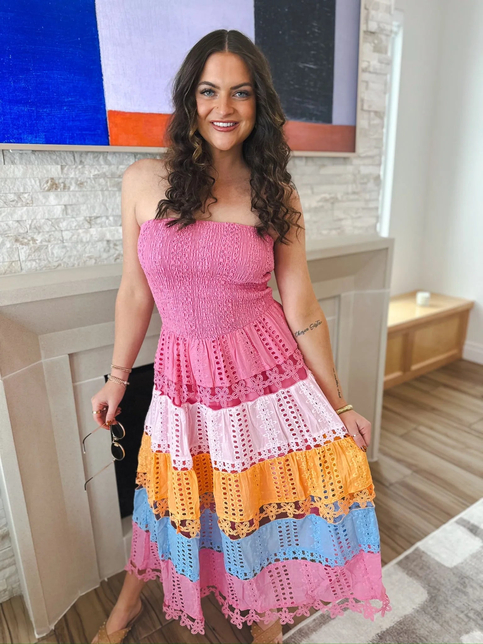 Woman in a pink, tiered, multi-eyelet lace midi dress with smocked bodice. The dress features stripes of pink, light pink