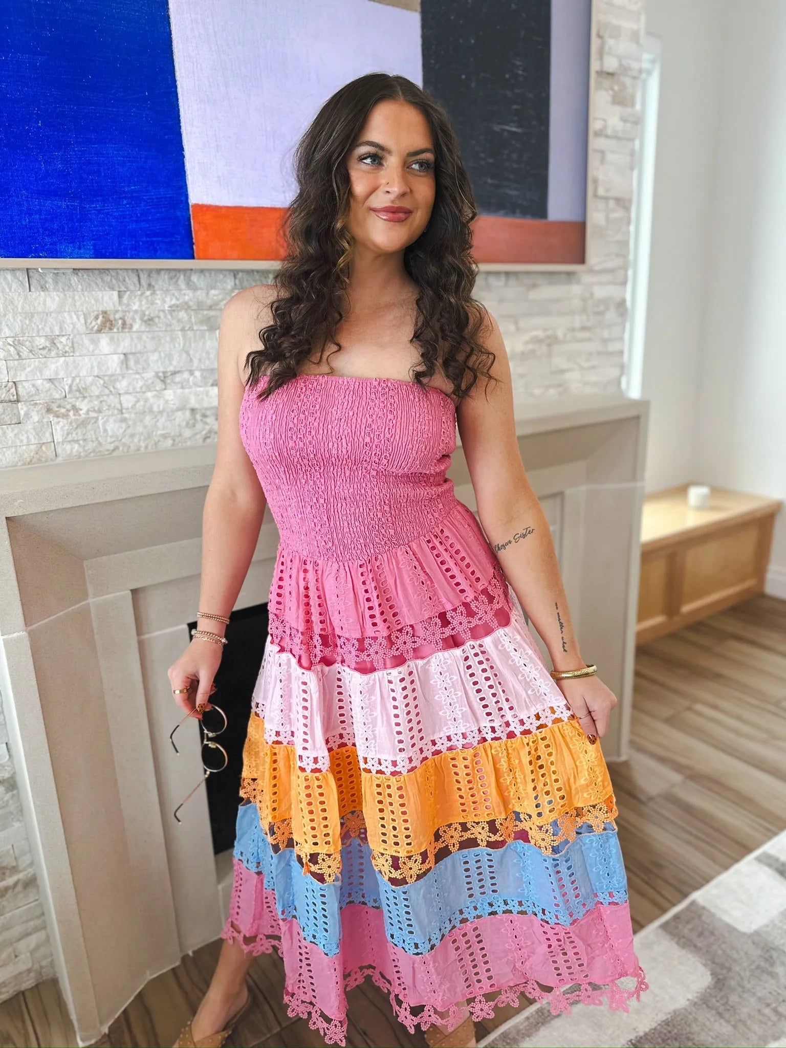 Woman wearing a pink strapless midi dress with eyelet lace details and colorful horizontal stripes in pink, light pink