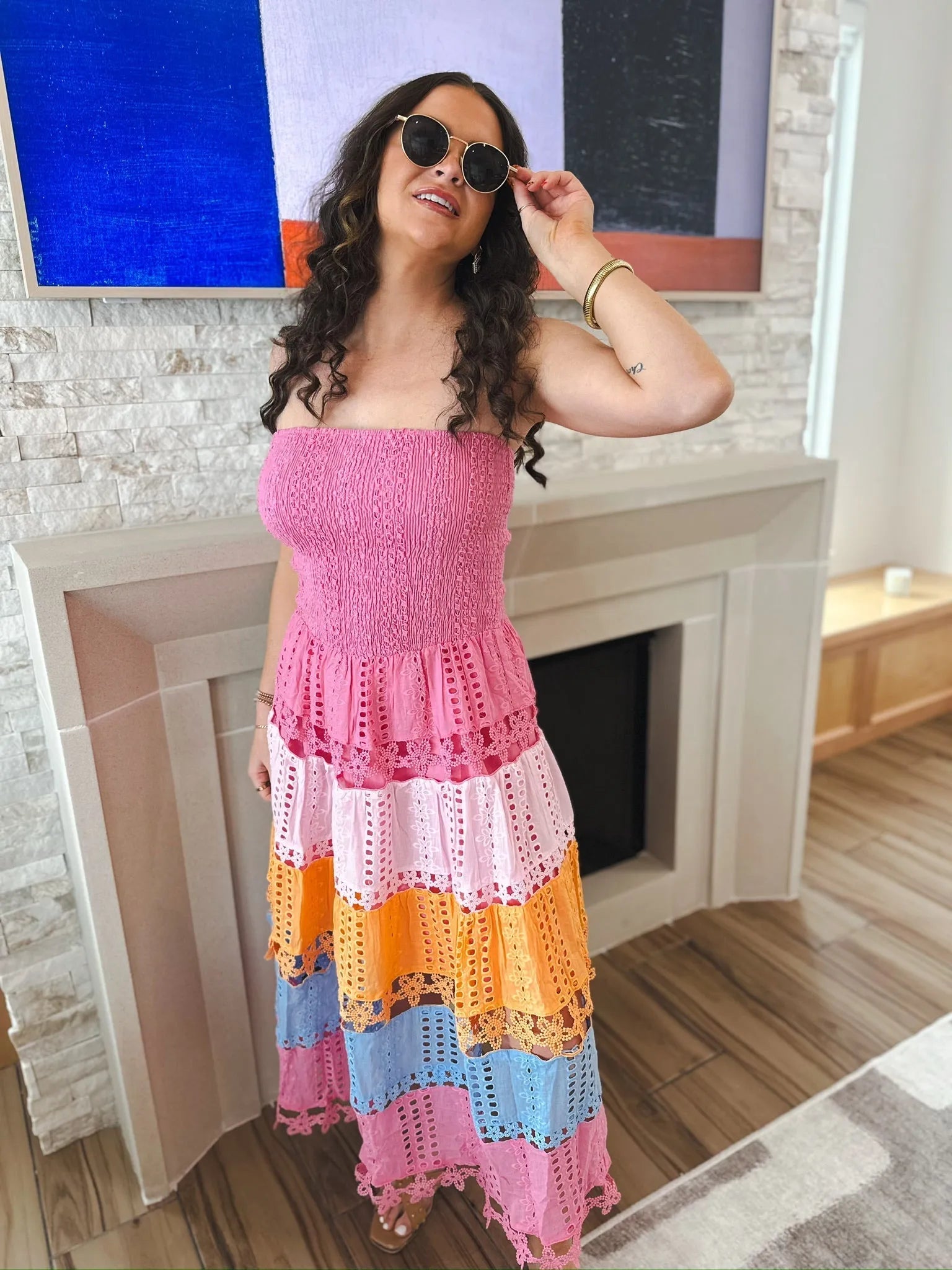 Woman wears a pink strapless midi dress with eyelet lace details and colorful horizontal stripes in pink, orange, and blue.
