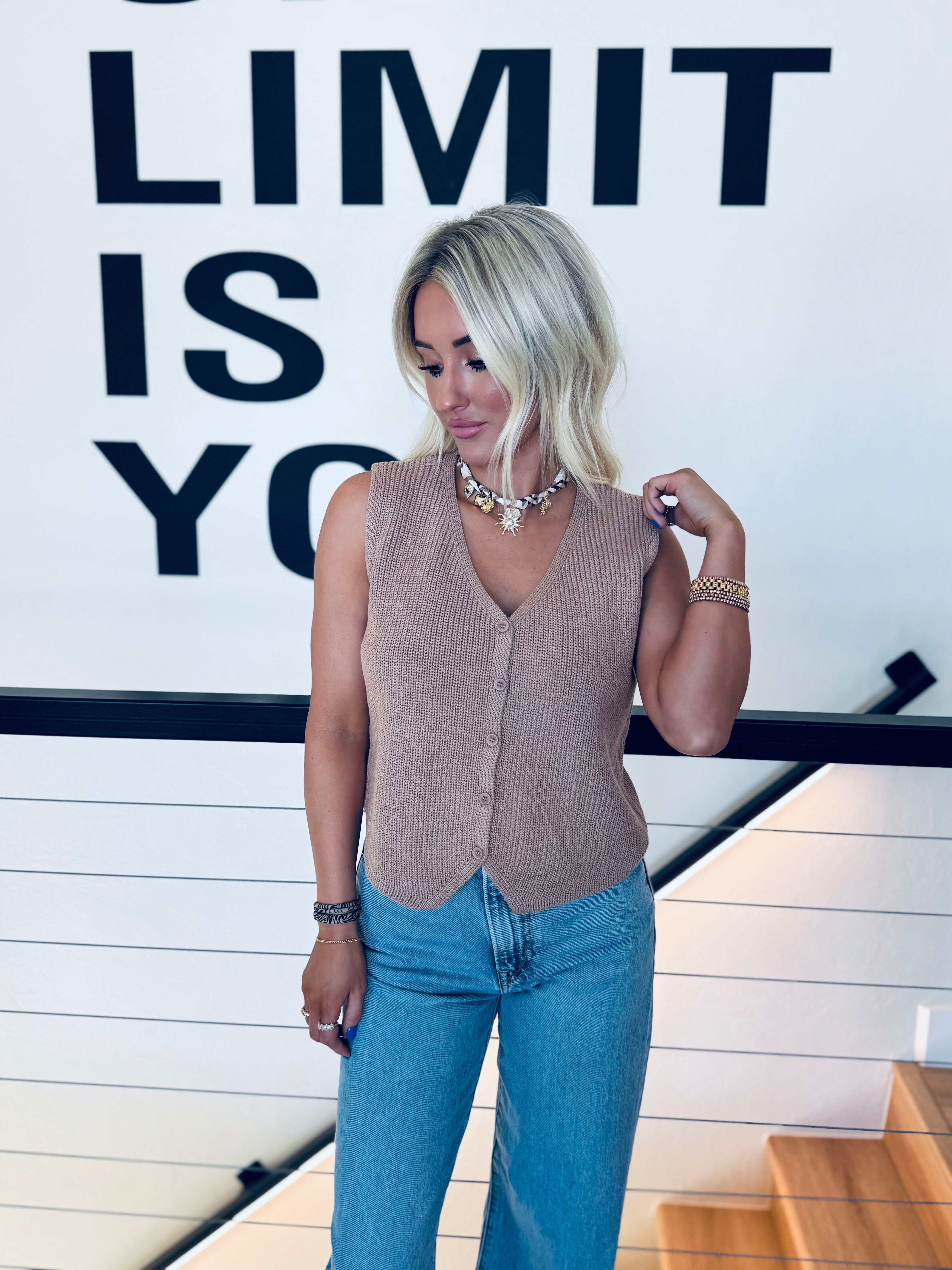 Taupe ribbed knit button-down sweater vest worn by a blonde woman with a beaded necklace and jeans.