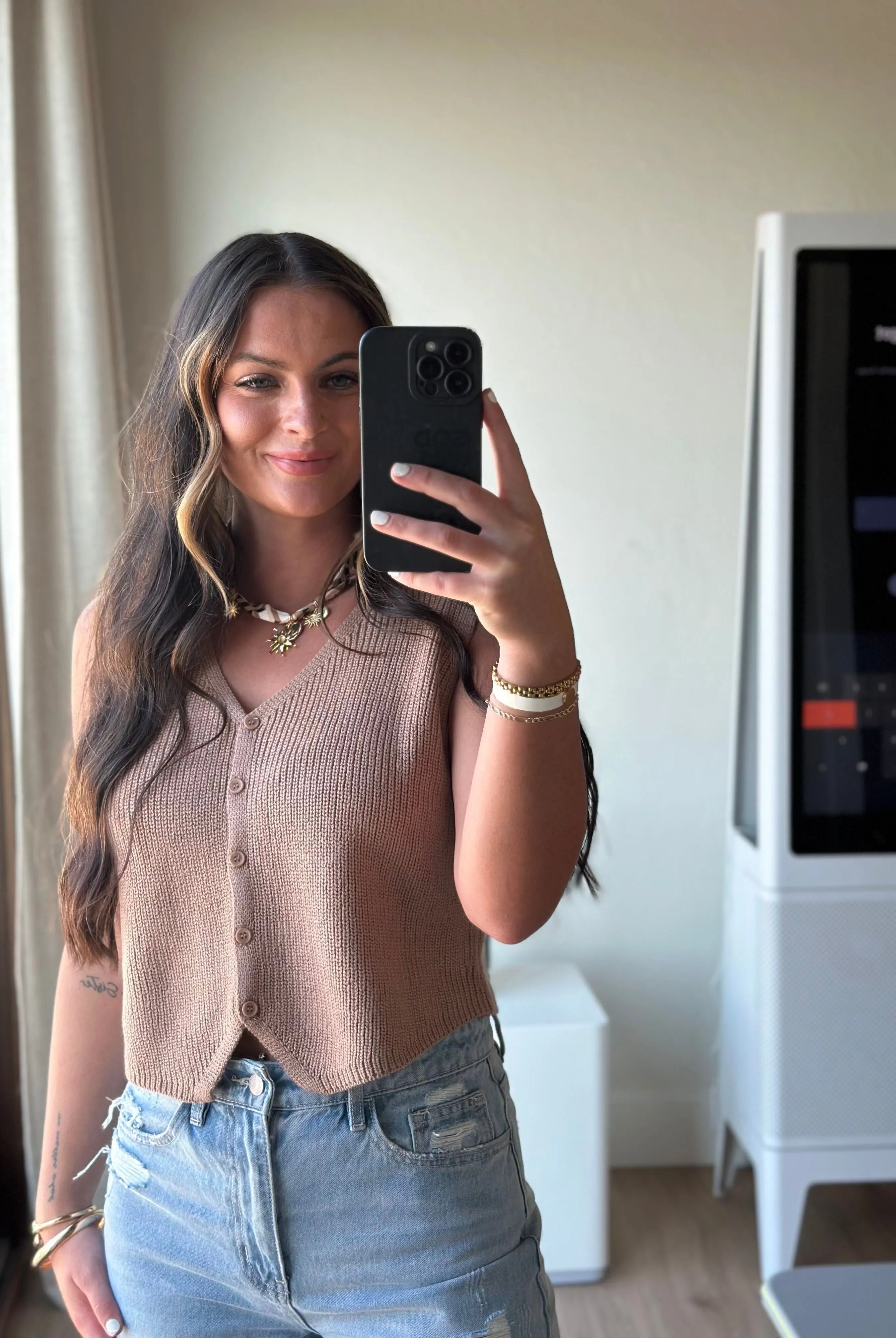 Taupe ribbed button-down sweater vest with a V-neck, worn by a woman in distressed denim shorts.