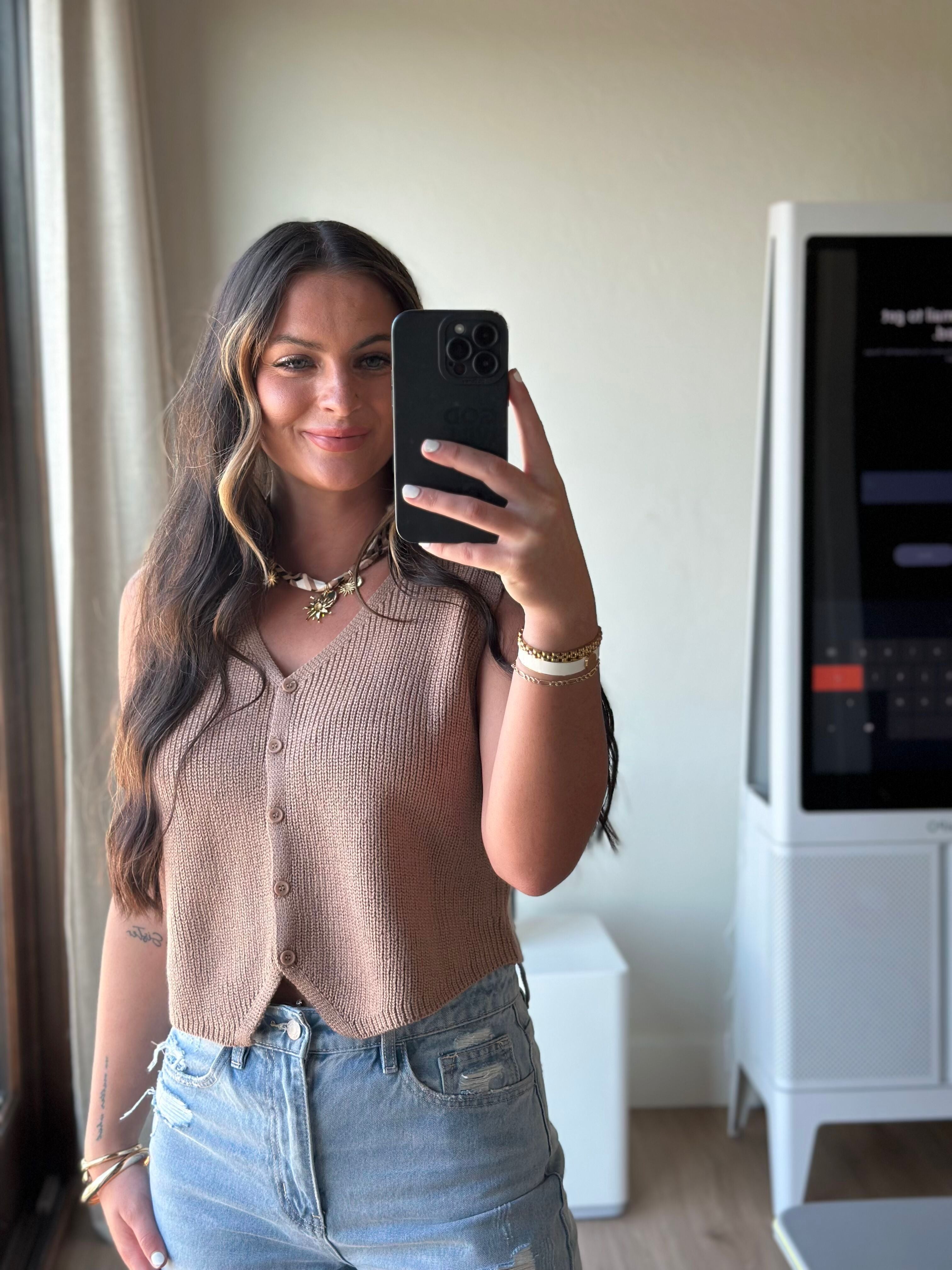 Taupe ribbed button-down sweater vest with a V-neck, worn by a woman in distressed denim shorts.