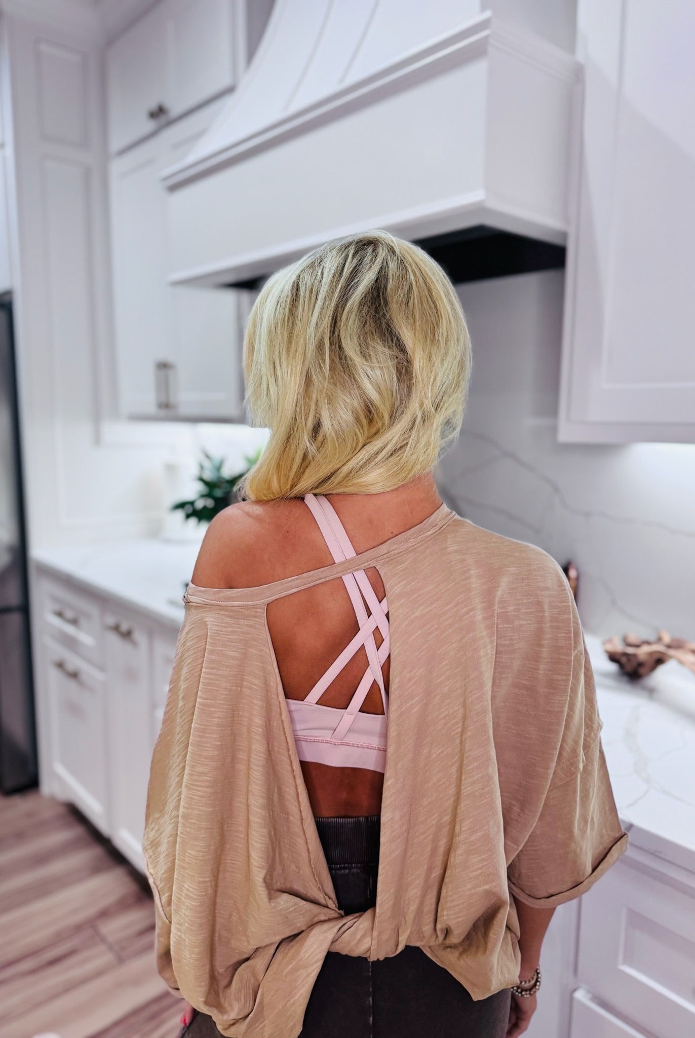 Taupe twist back cropped tee showing pink strappy bra. Back view of woman in a taupe shirt with cutouts.