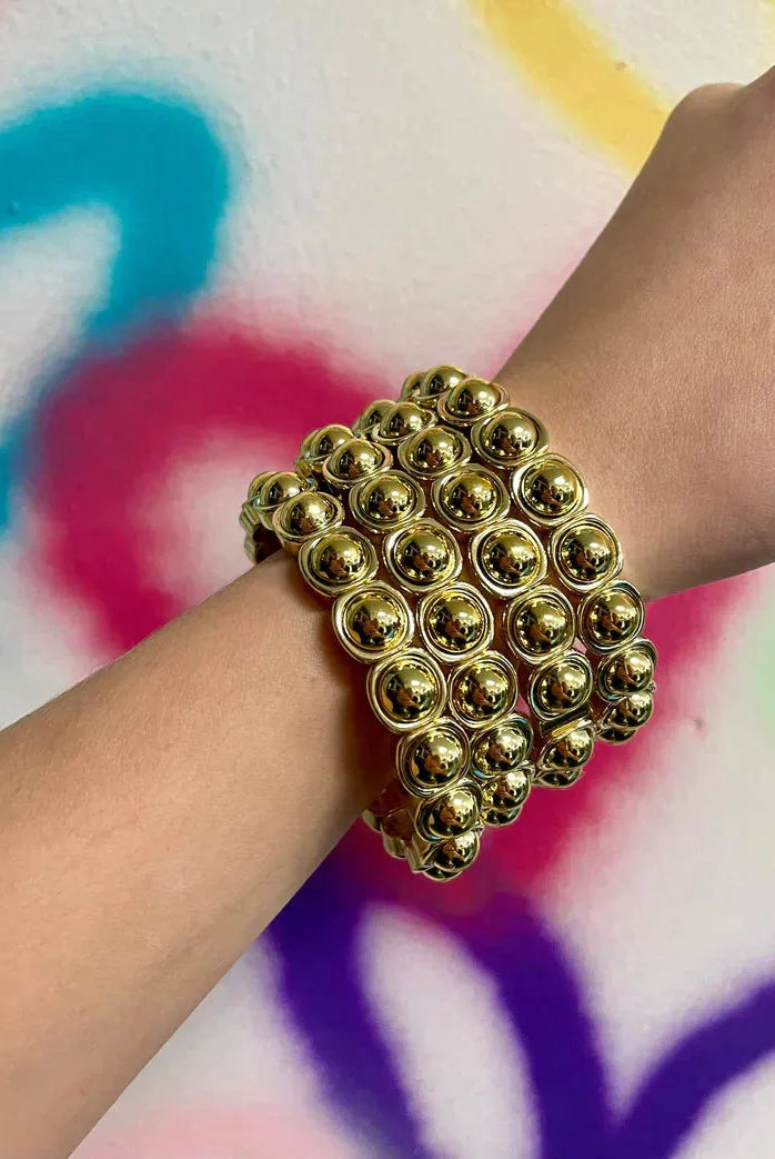 Taylor Shaye Pardi Gold Bracelet: A wide, multi-strand gold bracelet featuring rows of polished, spherical beads on a wrist.