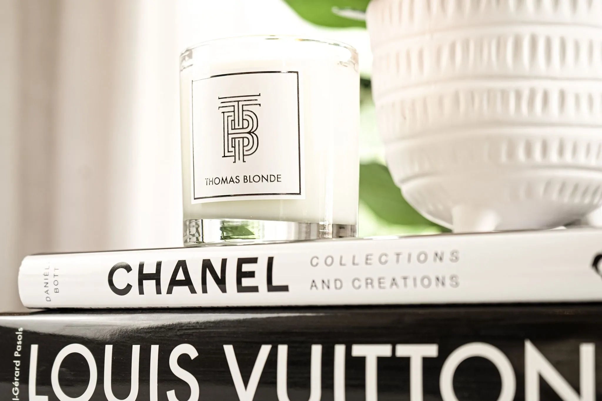 Thomas Blonde signature soy wax candle in glass jar with silver rim, on top of Chanel book.
