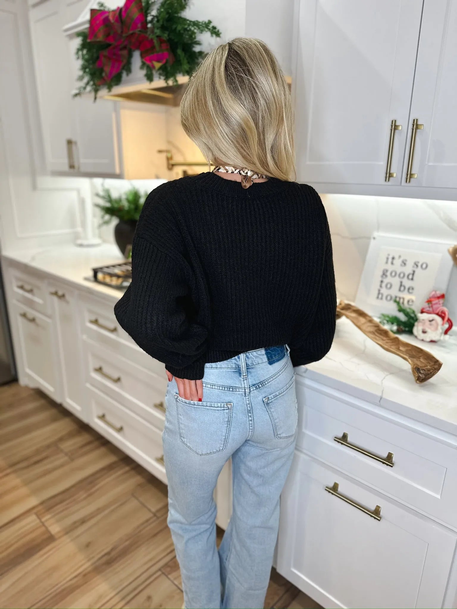 Back view of a woman wearing a black ribbed sweater and light wash, straight-leg jeans.