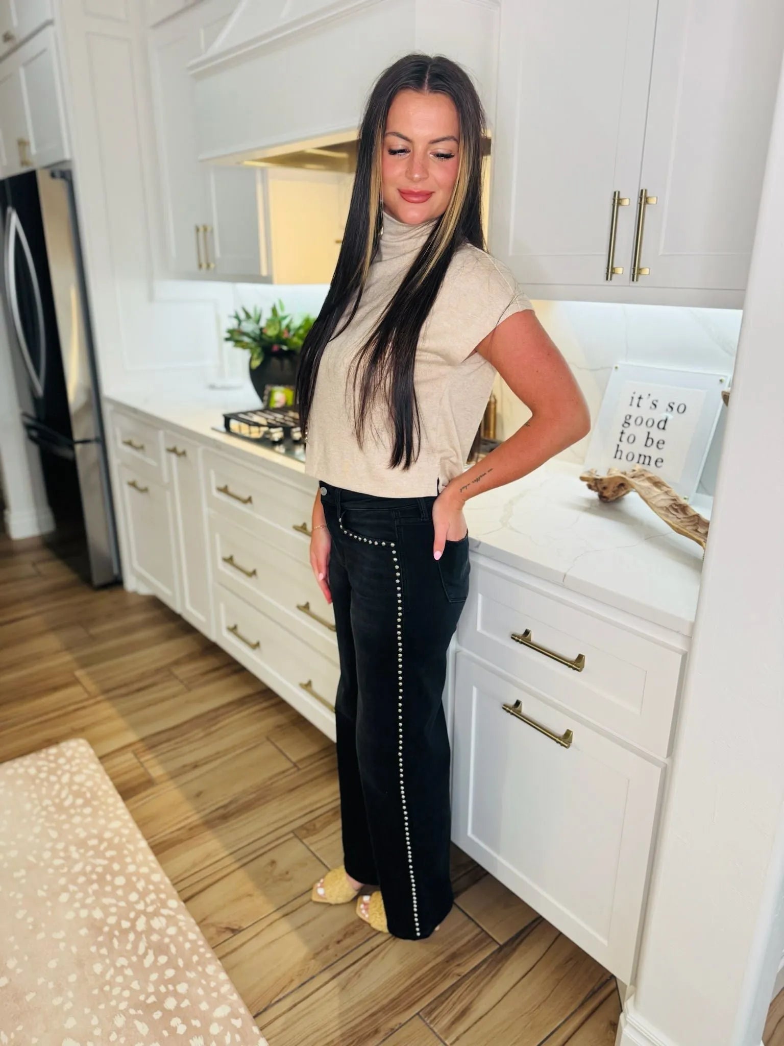 Vervet black high-rise wide-leg jeans with silver nailhead trim down the side seams, worn by a woman in a tan turtleneck
