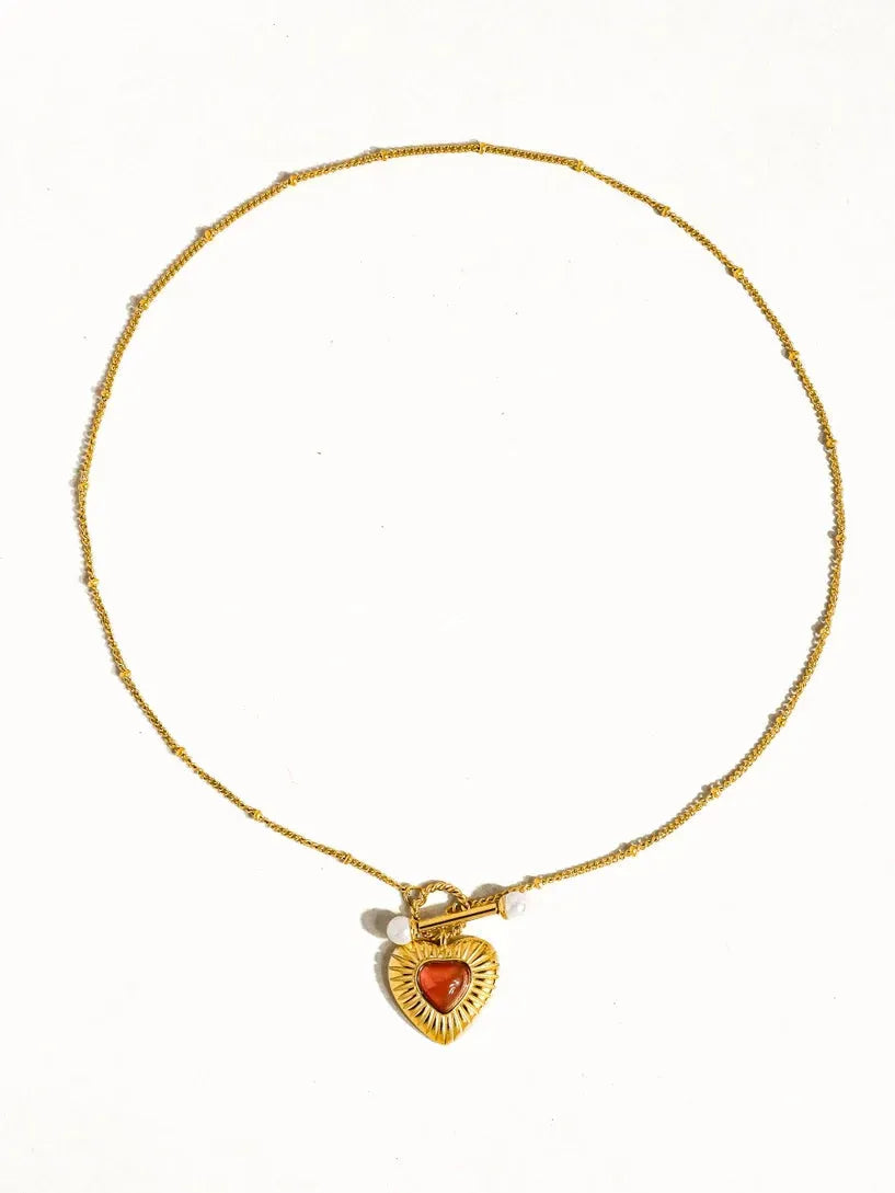 Gold necklace with beaded chain, toggle clasp, and a vintage-inspired heart locket featuring an orange agate stone.