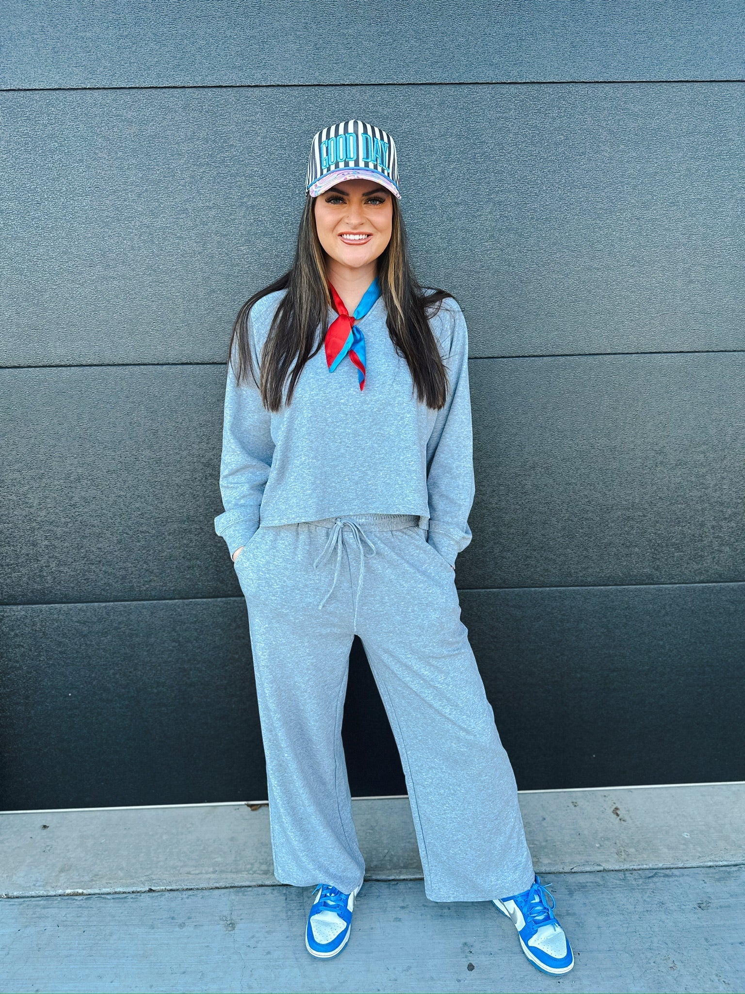 Woman wearing a V-neck heather grey matching sweat set with a drawstring waist, paired with a striped cap and red and blue