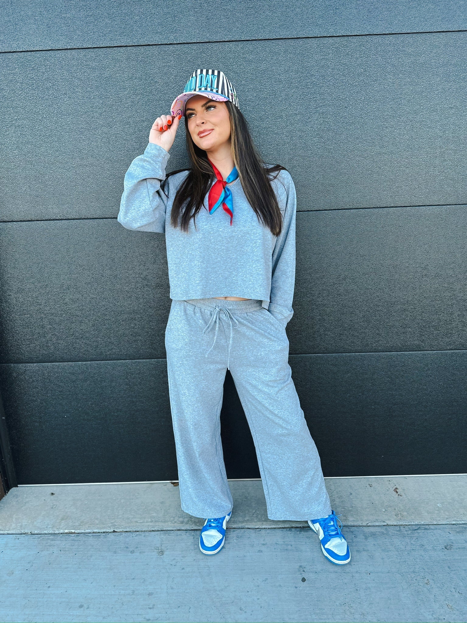 Woman wearing a heather grey cropped sweatshirt and wide-leg sweatpants with a red and blue scarf and striped cap.