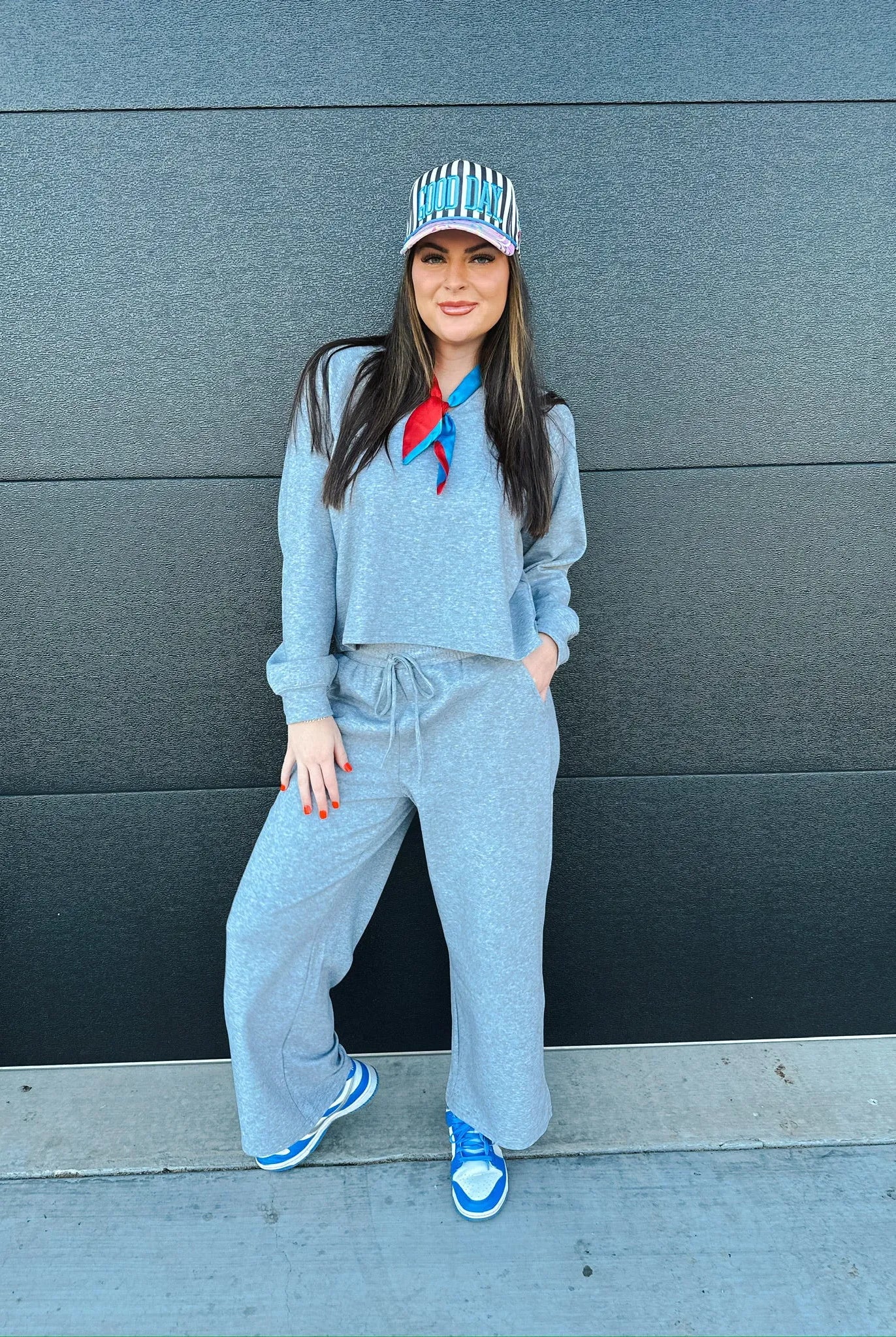 Woman wearing a heather grey V-neck cropped sweatshirt and wide-leg sweatpants, accessorized with a striped baseball cap
