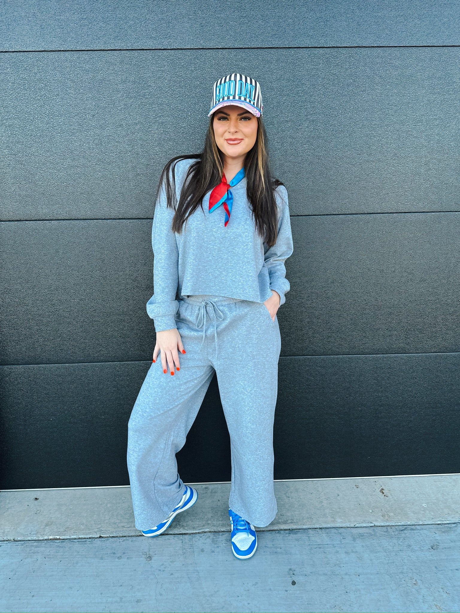 Woman wearing a heather grey V-neck cropped sweatshirt and wide-leg sweatpants, accessorized with a striped baseball cap