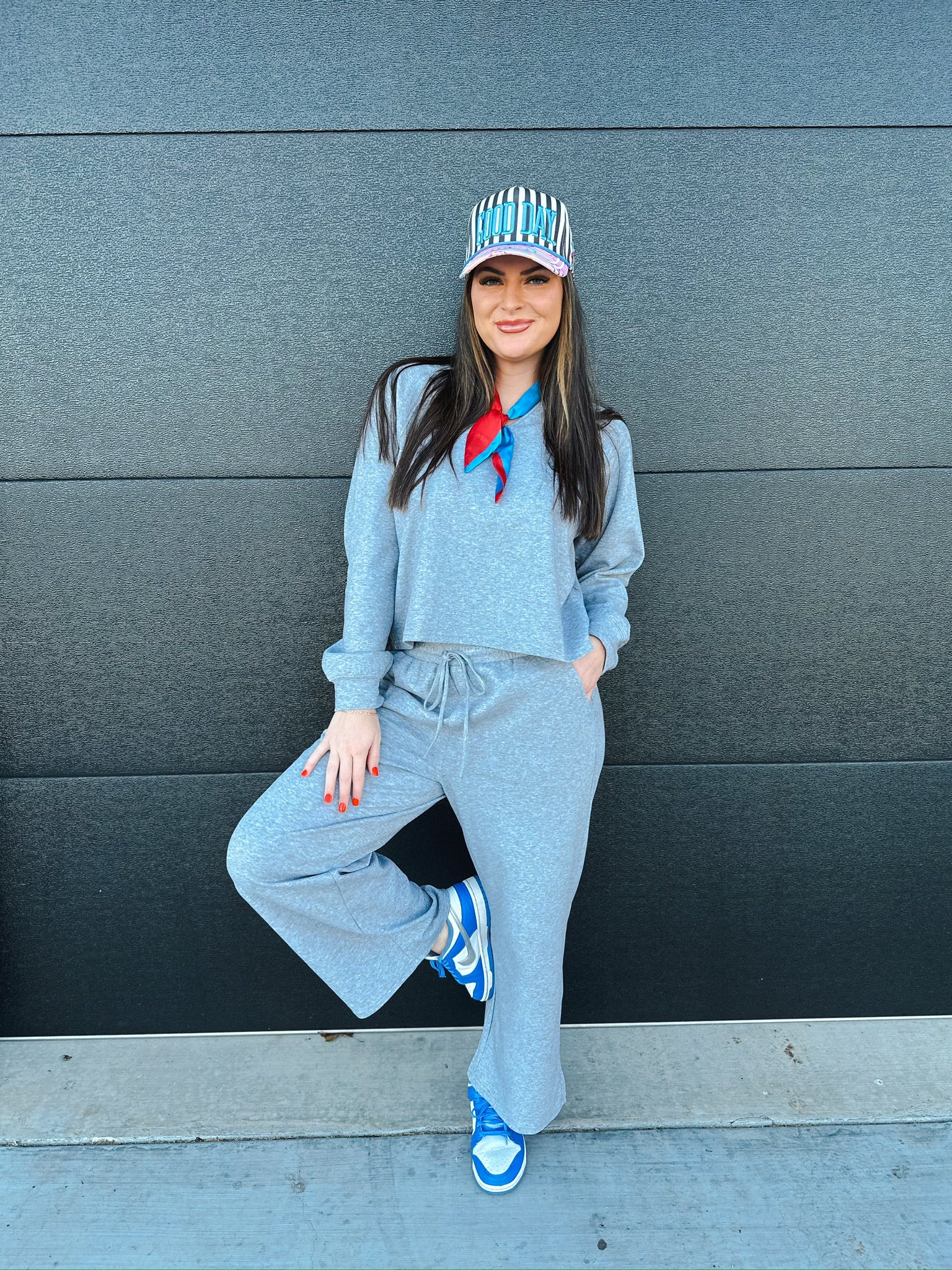 Woman wearing a heather grey v-neck loungewear set, wide-leg pants, and blue sneakers, with a striped cap and red/blue