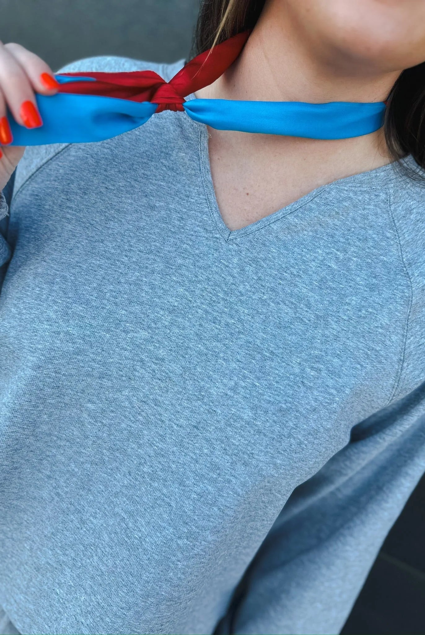 Heather grey v-neck long sleeve top with a red and blue scarf tied around the neck.