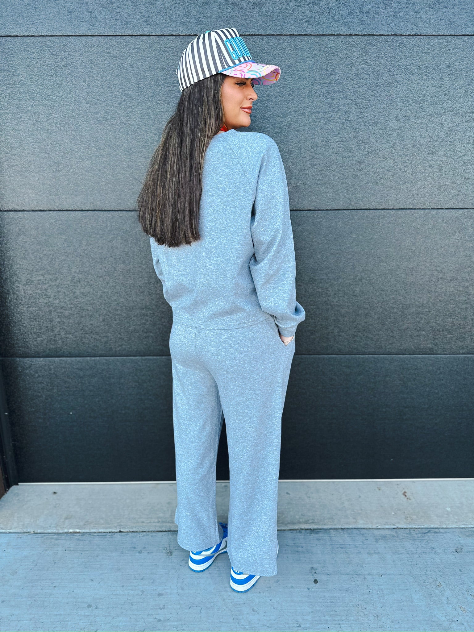 A woman wears a heather grey V-neck sweatshirt and matching wide-leg sweatpants, paired with a striped baseball cap and